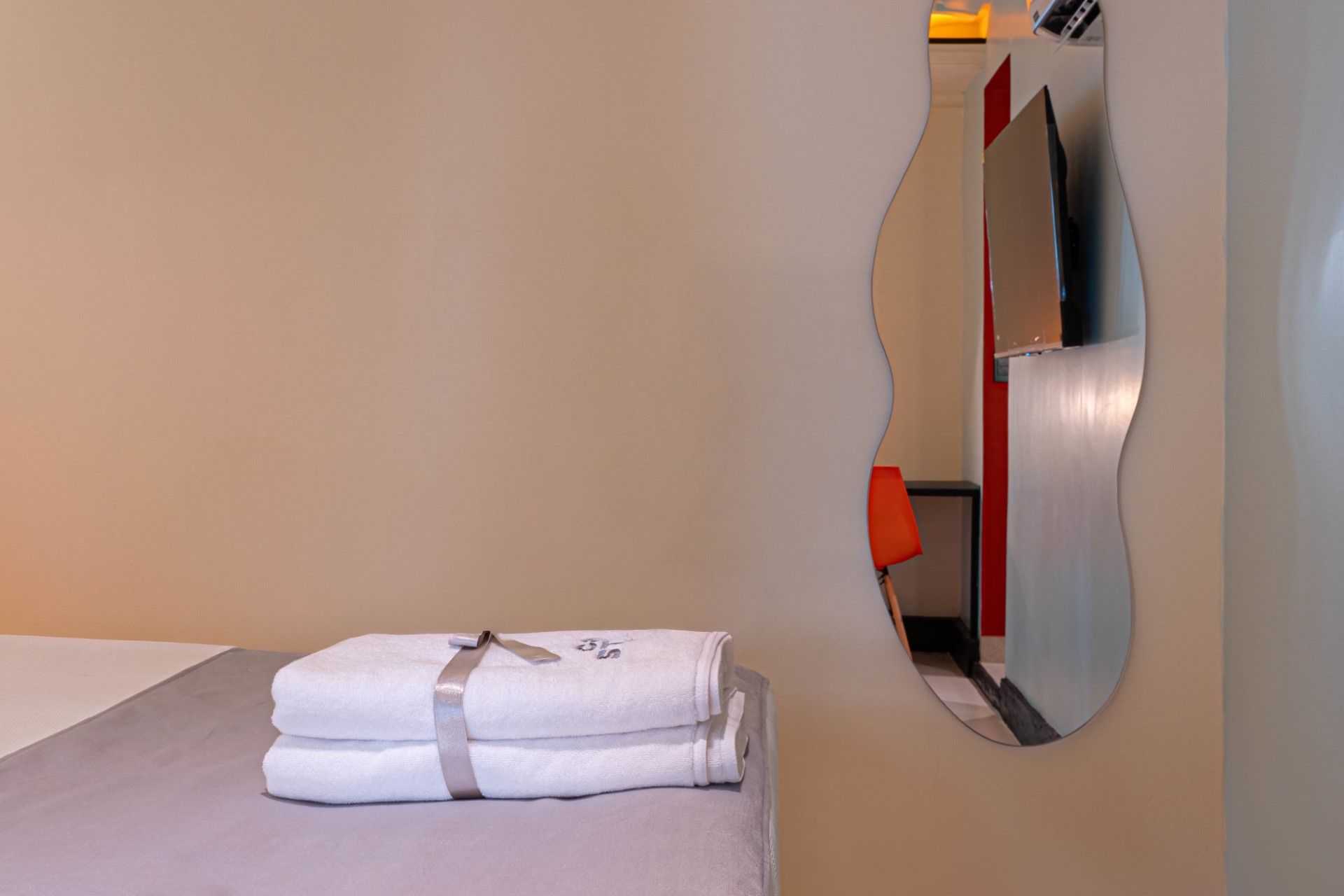 Toallas blancas sobre una cama; un espejo ondulado cuelga de una pared, reflejando el interior de una habitación.