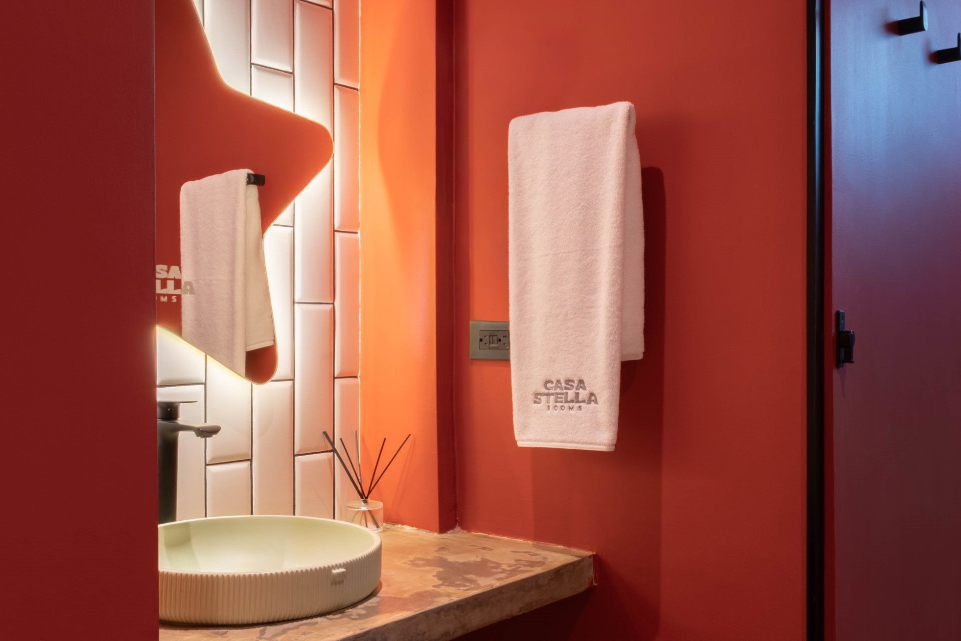 Baño rojo con azulejos blancos, lavabo redondo y toalla en la pared.