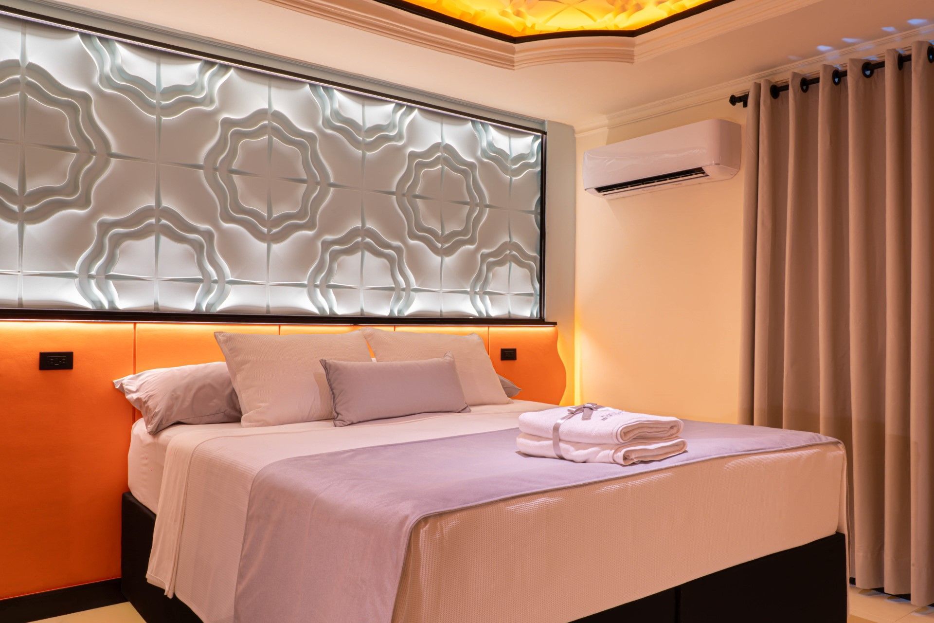 Dormitorio con cama, panel de pared estampado, cabecero naranja y aire acondicionado.