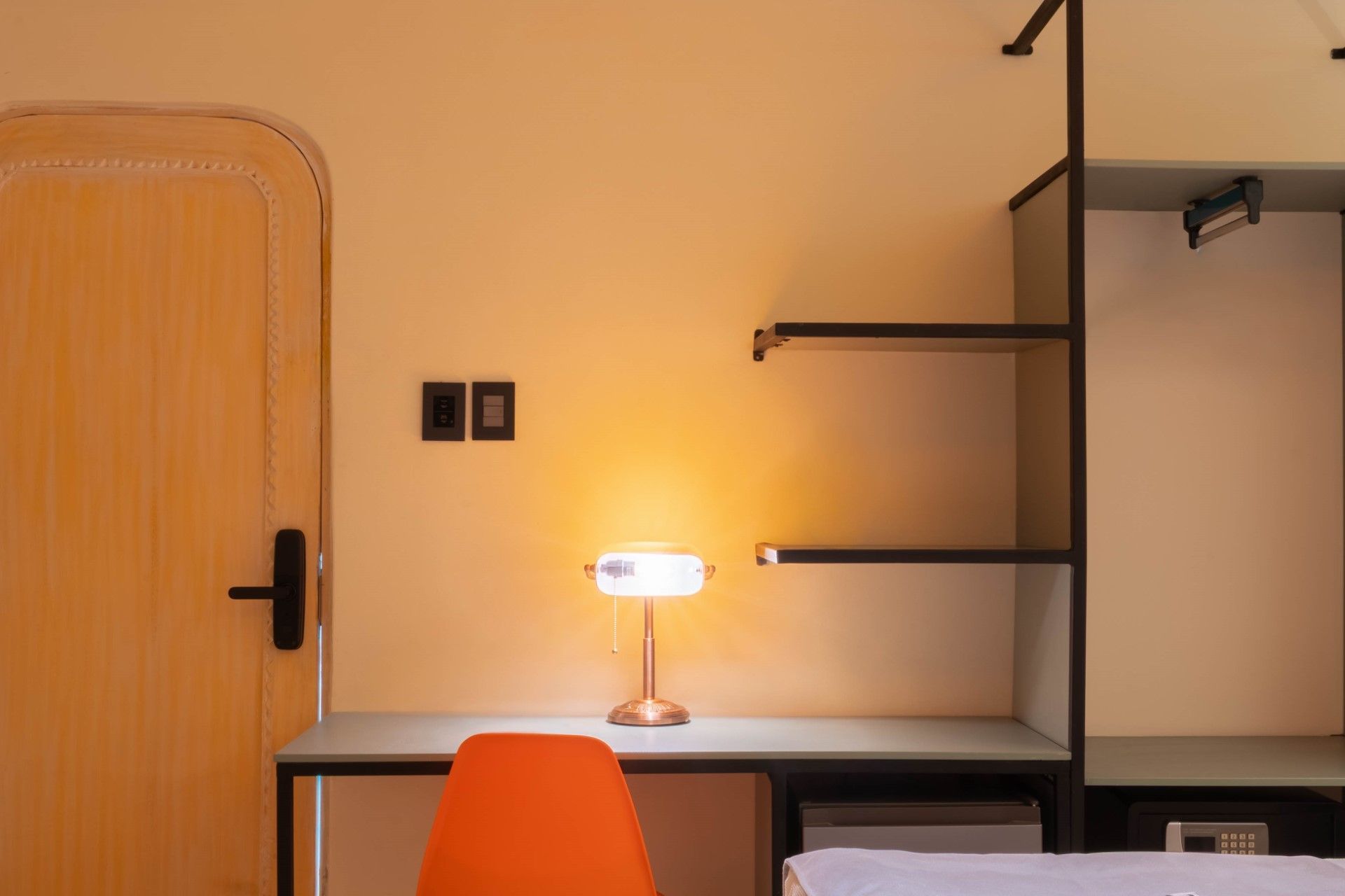 Escritorio con lámpara y silla naranja, junto a un armario abierto con estantes.