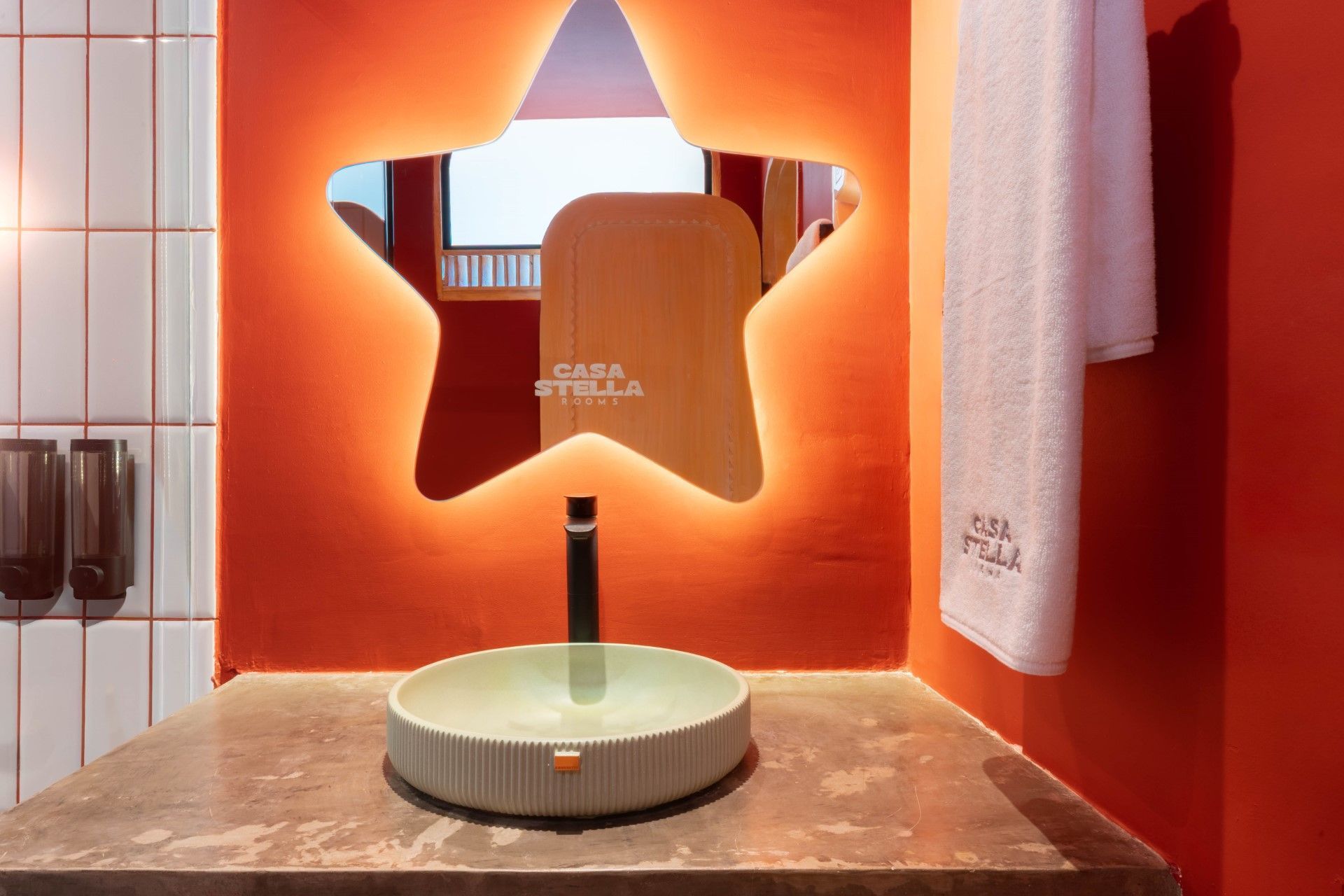Baño con espejo en forma de estrella, paredes naranjas, encimera gris y toalla blanca.