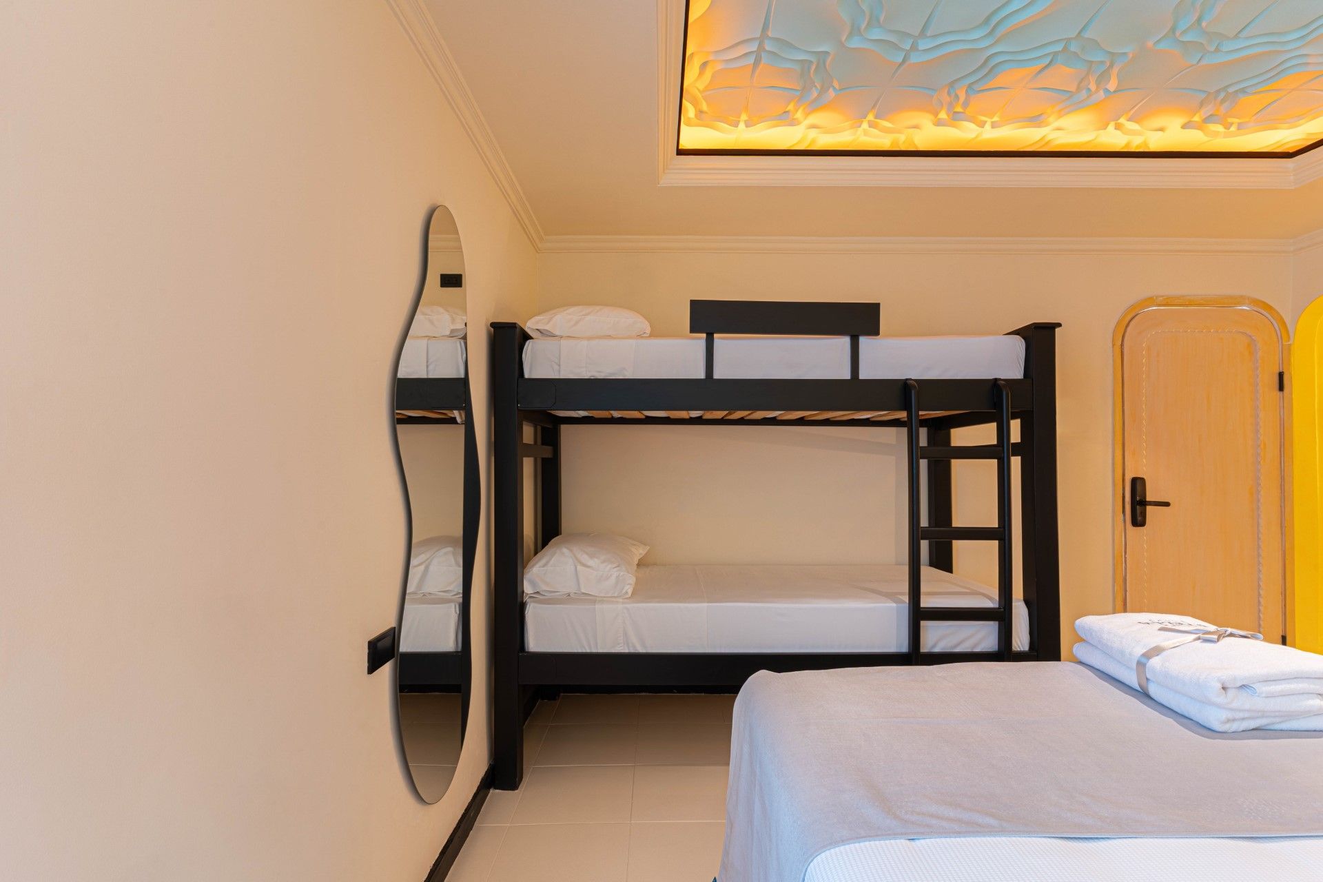 Dormitorio con litera negra, espejo y dos camas cubiertas con sábanas blancas.