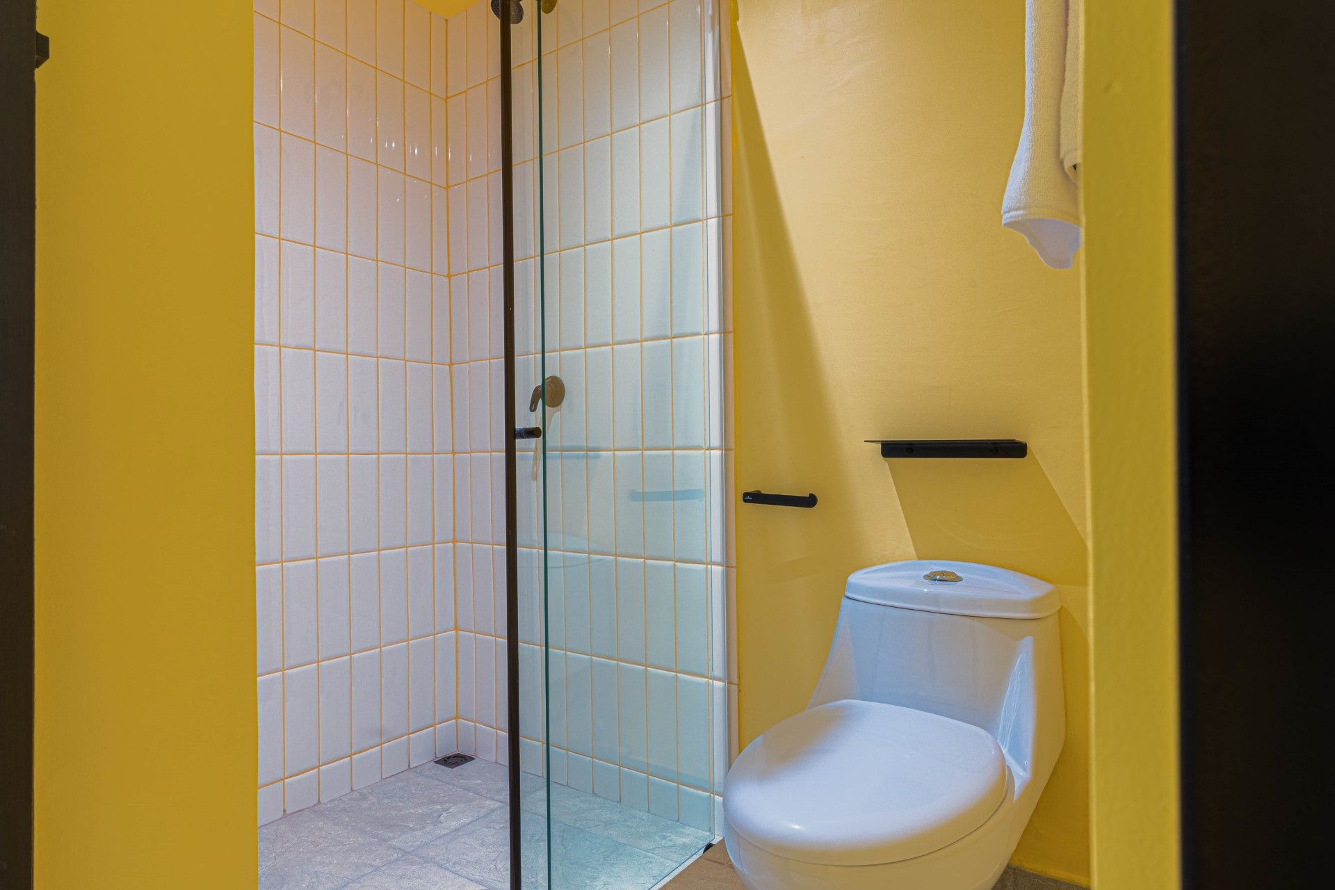 Cabina de ducha con puerta de cristal junto a un inodoro blanco en un baño de paredes amarillas.