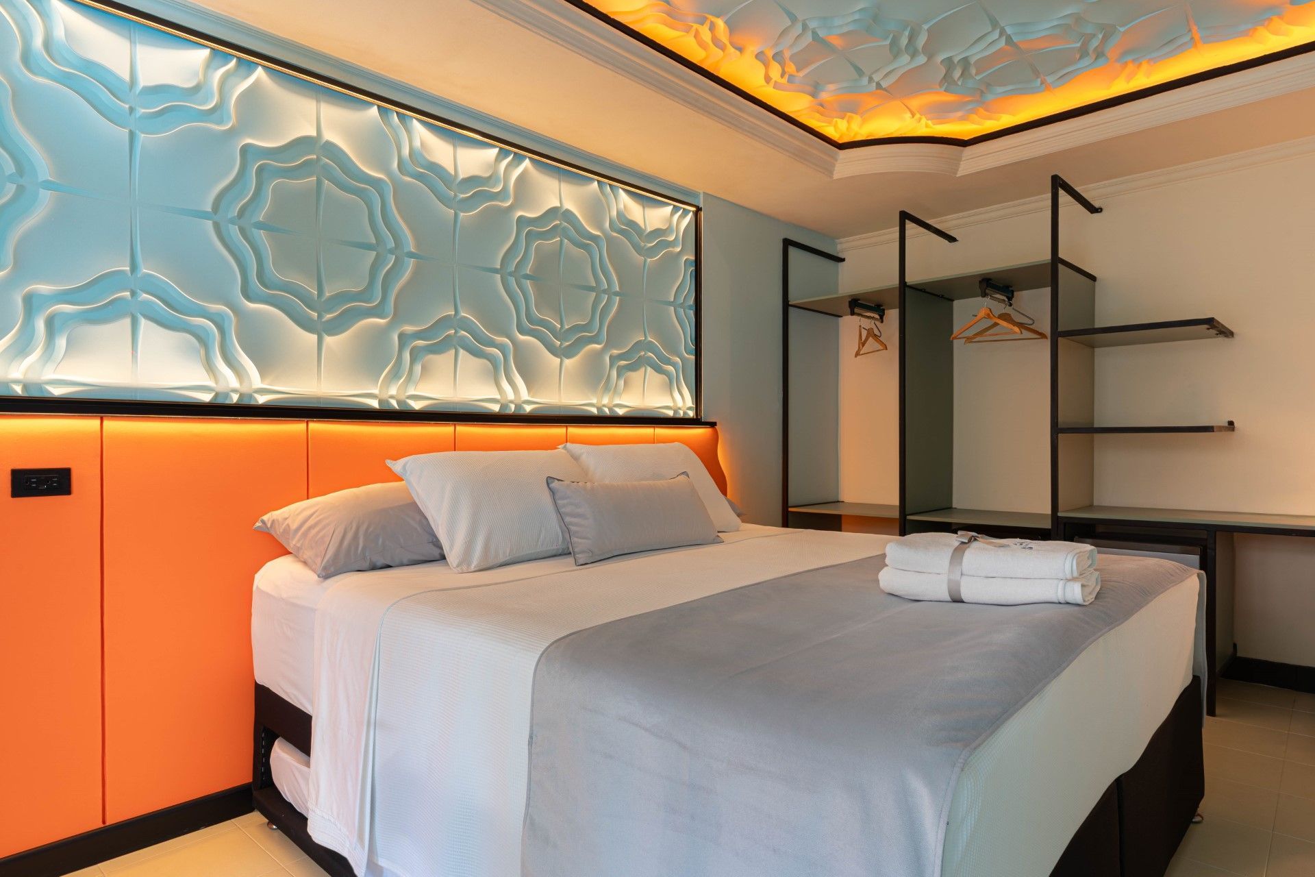 Dormitorio con cama, cabecero naranja, decoración de pared azul y armario abierto.