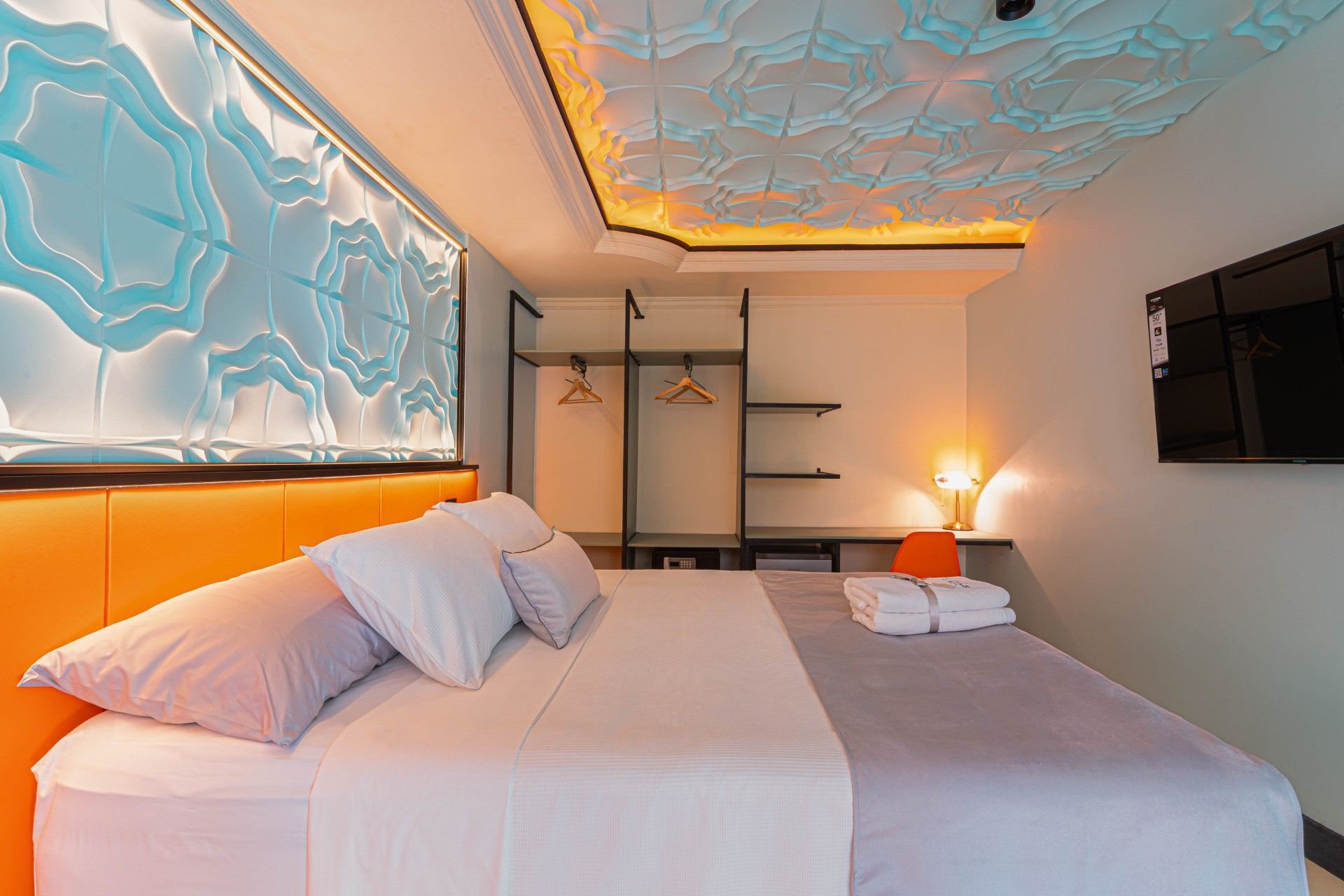 Dormitorio con cabecero naranja, cama, pared decorativa, tv y diseño de techo único.