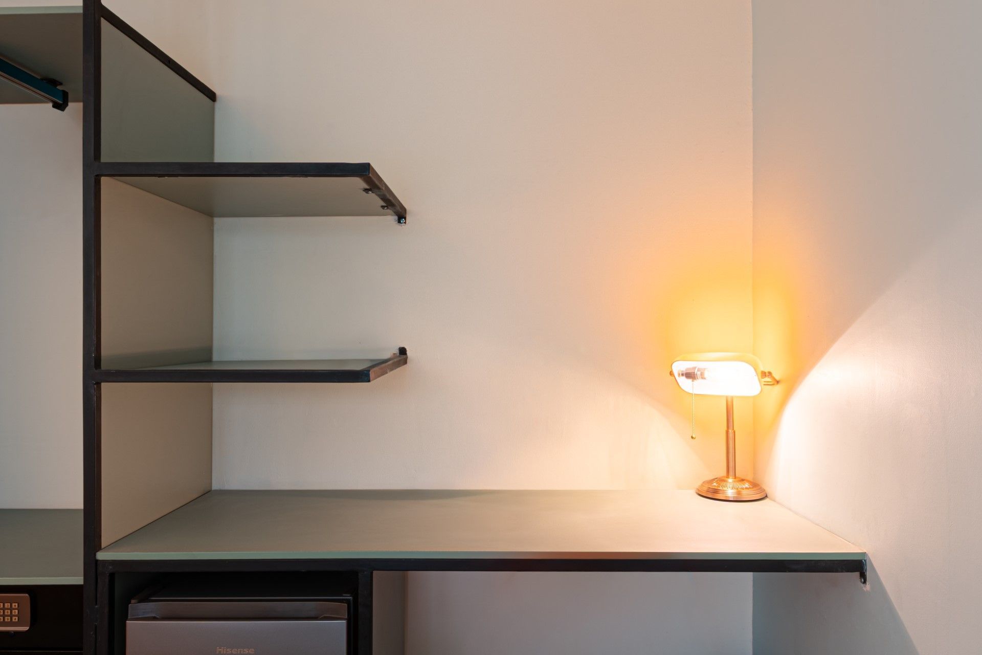 Escritorio empotrado con estantes. Una lámpara proyecta una cálida luz sobre el escritorio esquinero y la pared blanca.