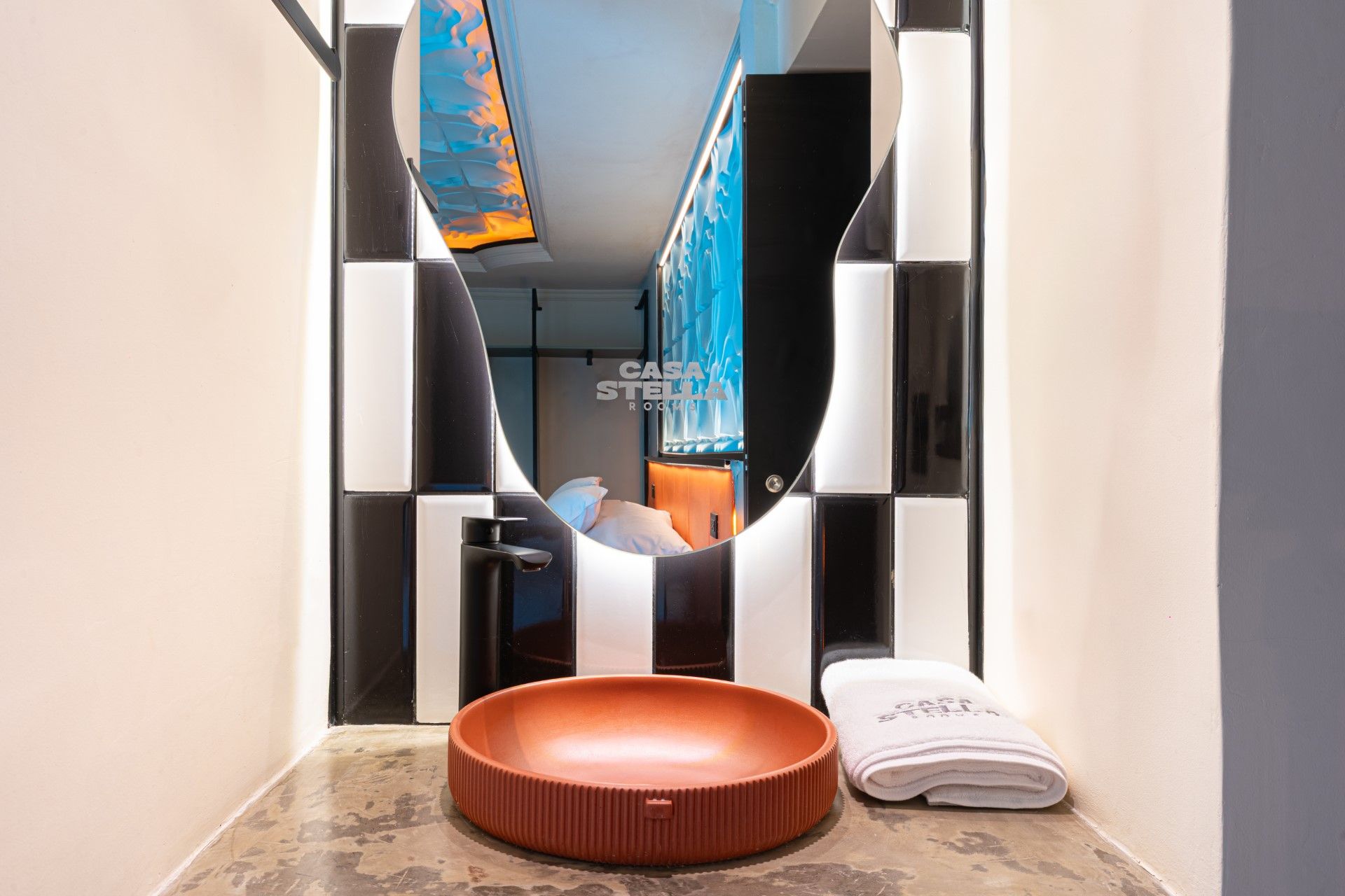 Lavabo de baño con cubeta marrón, grifo negro y espejo estampado enmarcado por azulejos blancos y negros.