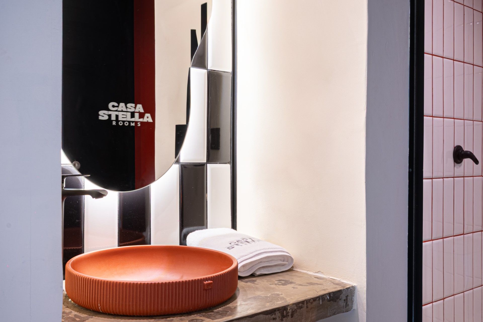 Baño con lavabo rojo, pared a cuadros blancos y negros, toalla y puerta.