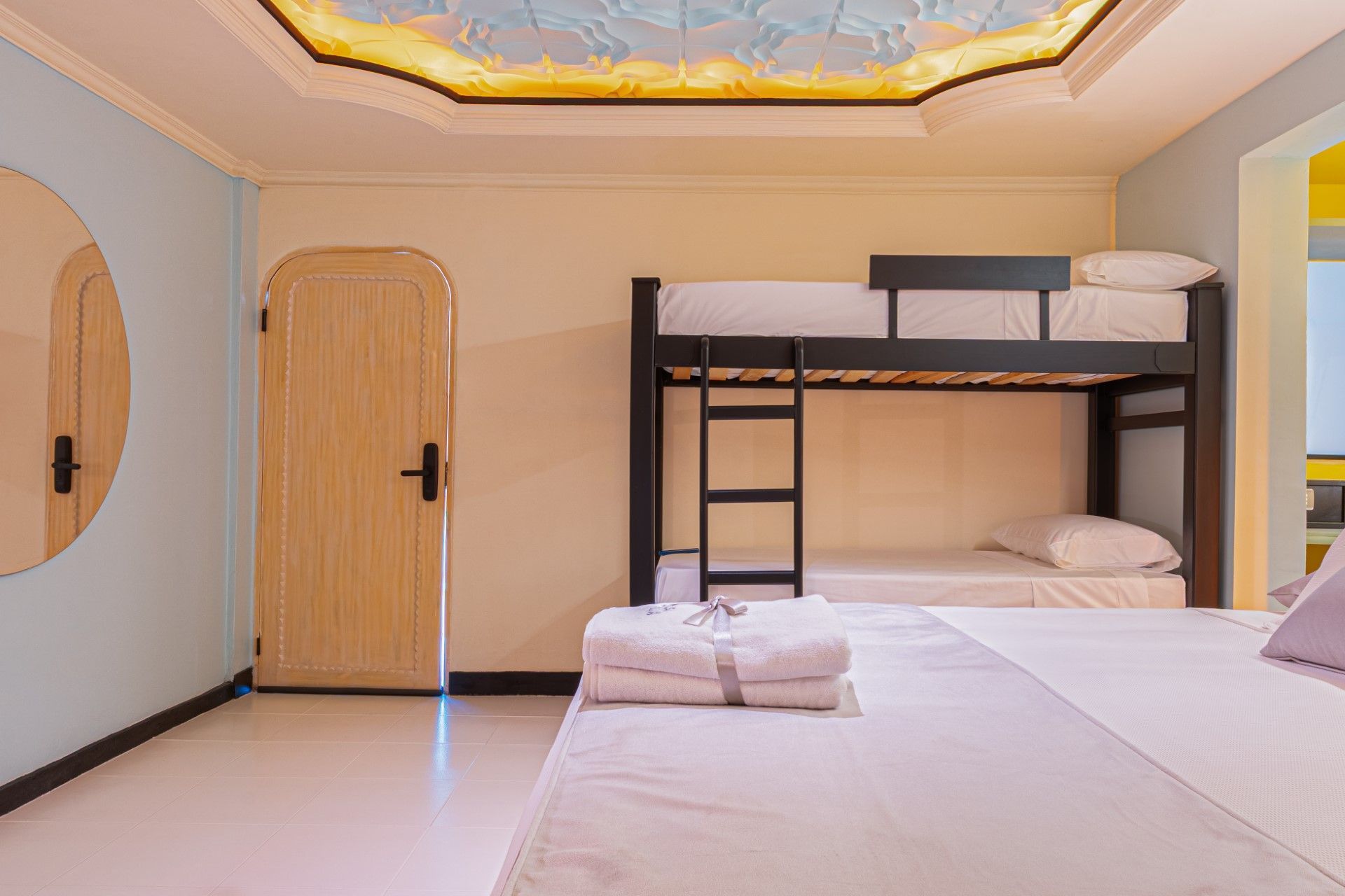 Dormitorio con literas, cama individual, espejo redondo y techo estampado.