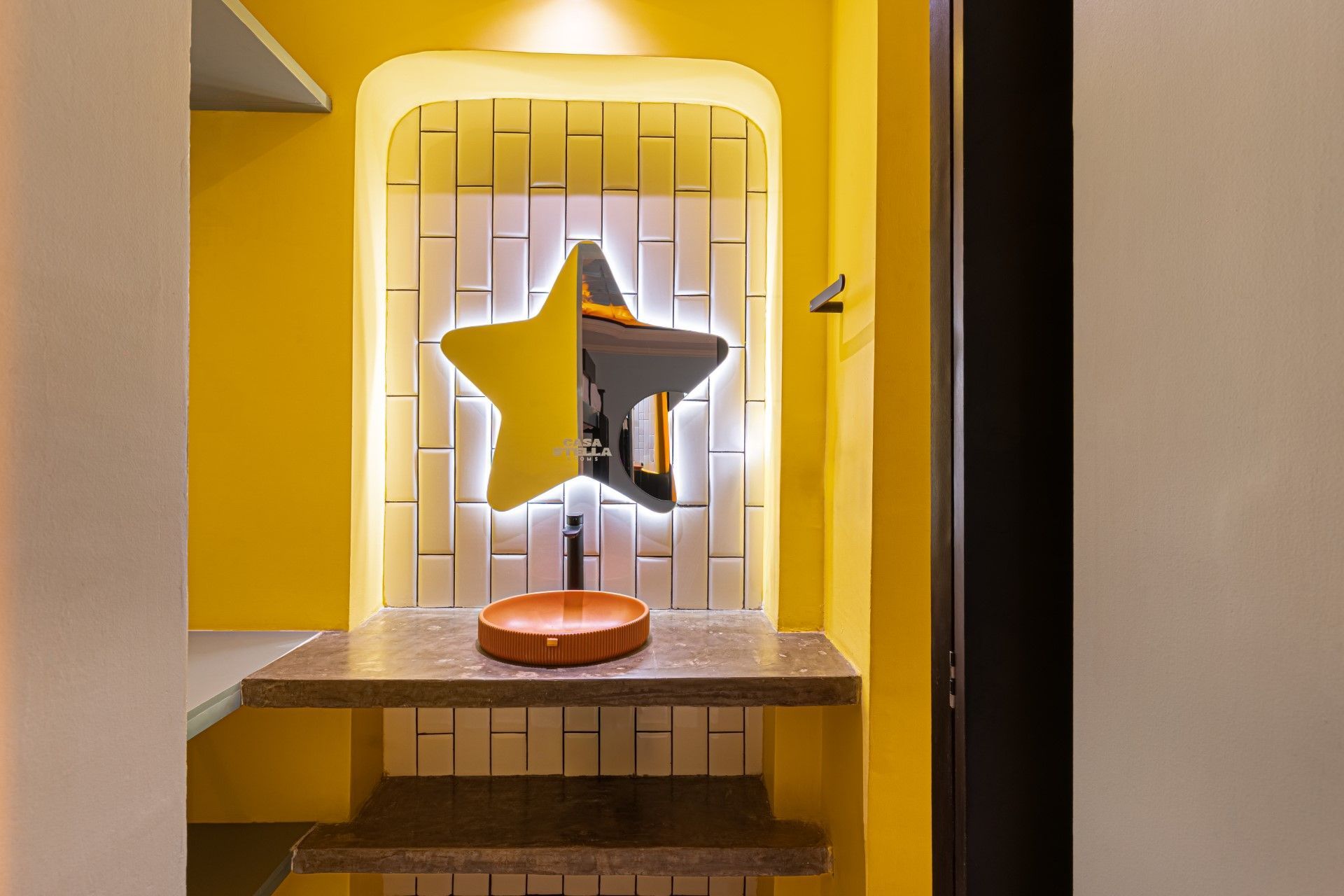 Baño amarillo con espejo en forma de estrella, lavabo marrón y salpicadero de azulejos.