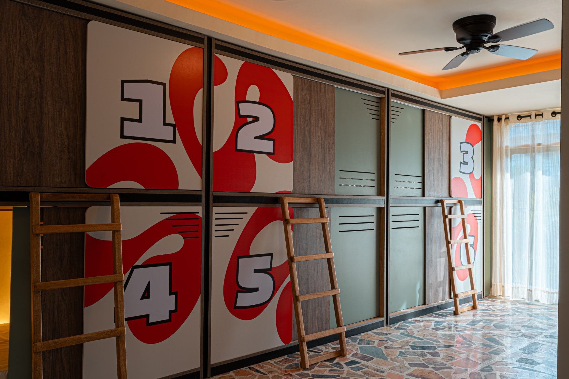 Habitación con literas con números pintados del 1 al 5, escaleras de madera y ventilador de techo.