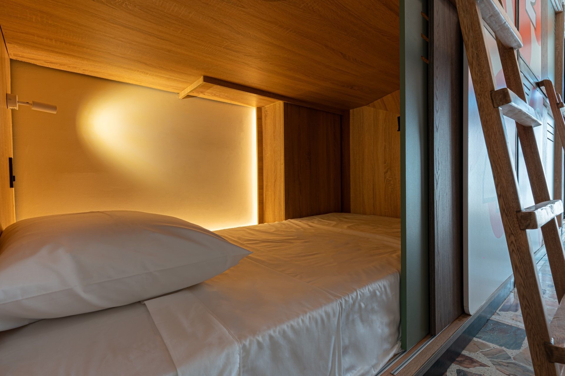 Acogedora litera con iluminación tenue y escalera. Estructura de madera, ropa de cama blanca y almohada.