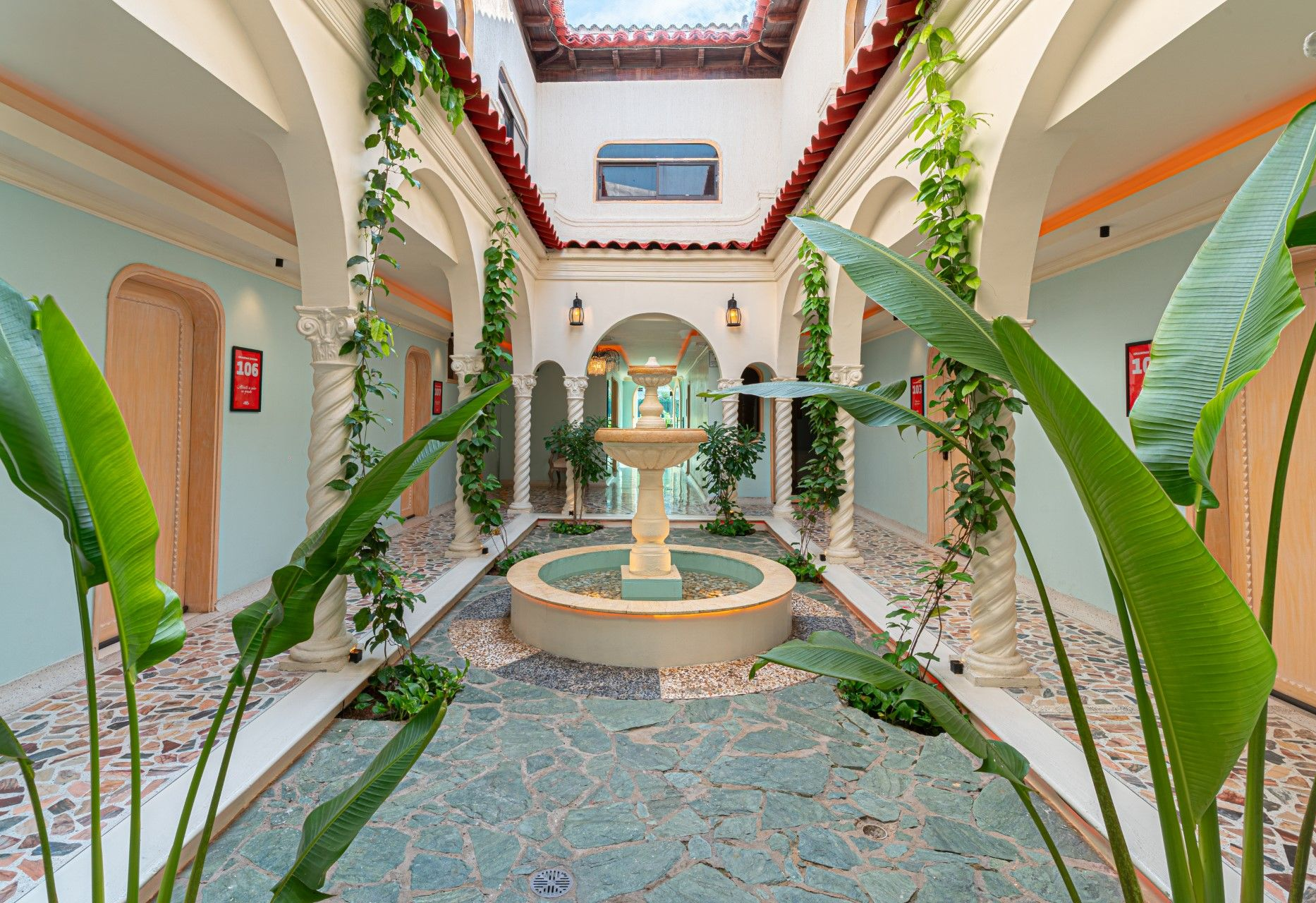 Patio con fuente, arcos y plantas trepadoras. Suelo de baldosas turquesas y paredes azules.