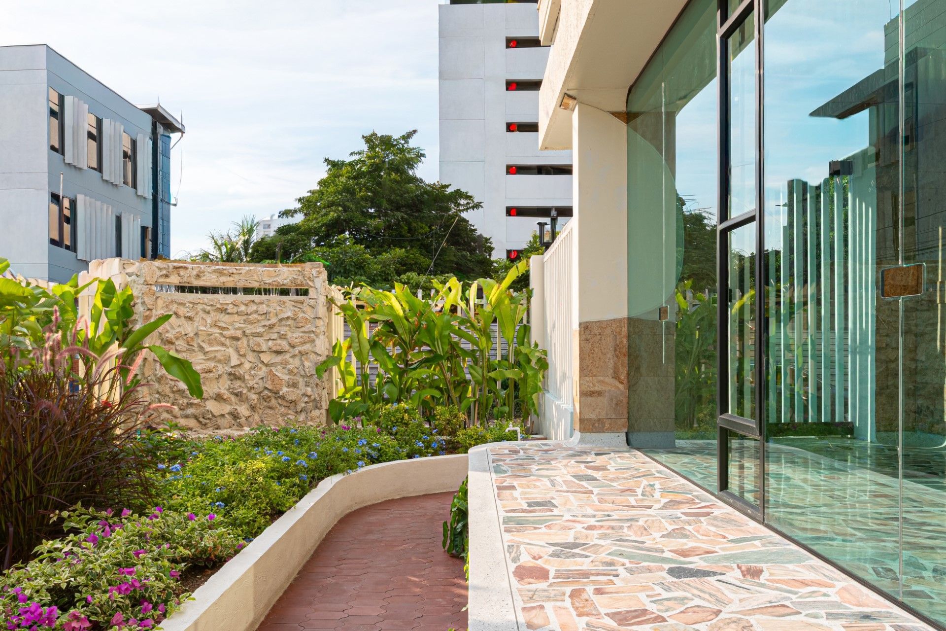 Una pasarela serpentea a través de un jardín con un edificio y ventanas al fondo.
