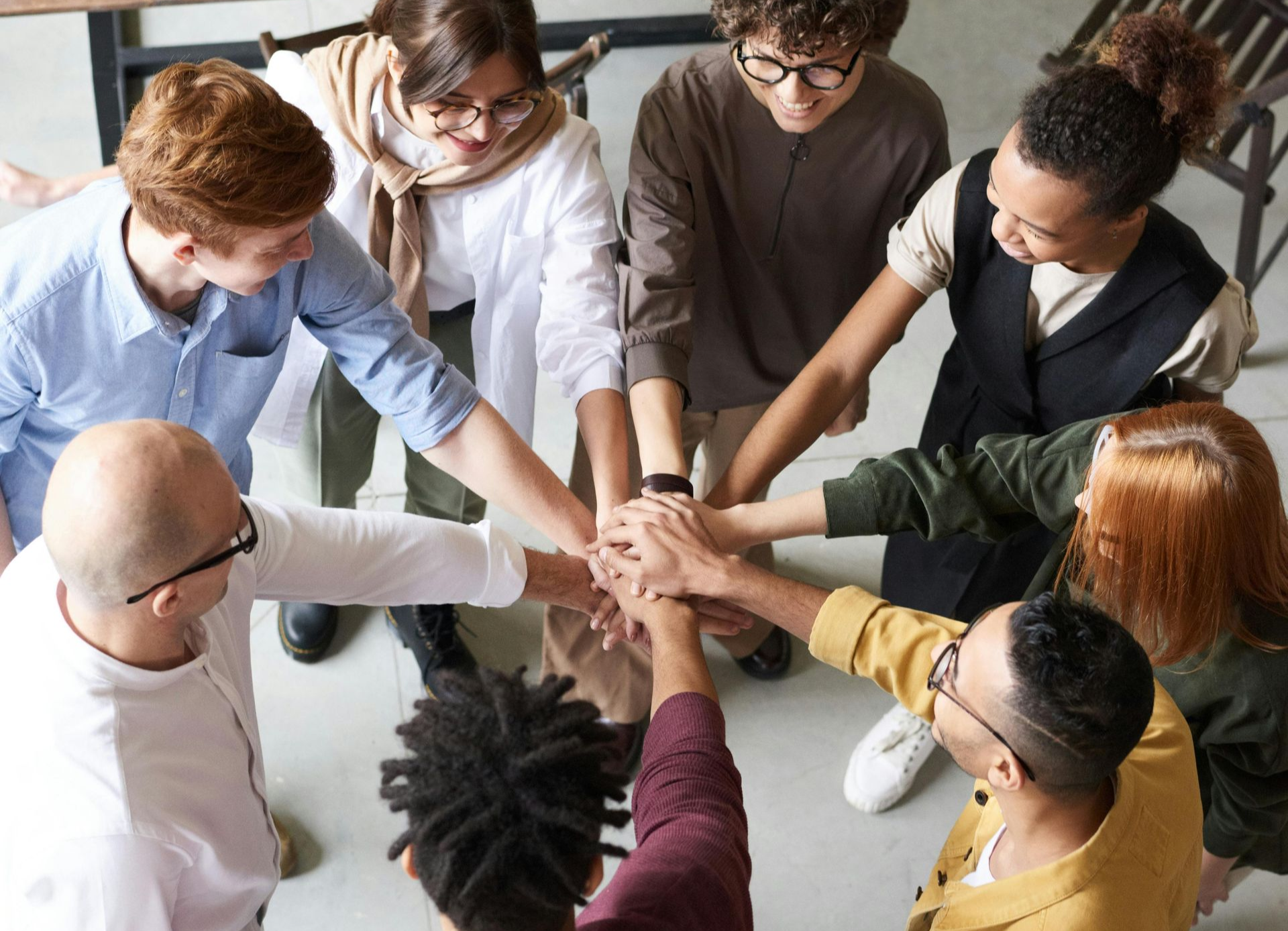 Personas con diversos tonos de piel, con los brazos apilados en un grupo, unidos y mostrando trabajo en equipo.