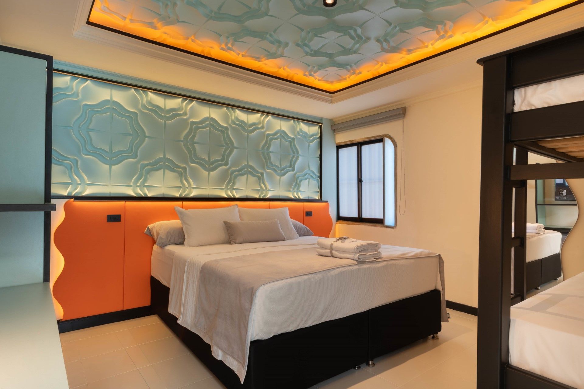 Dormitorio con cama doble, litera y pared con acento turquesa. Cabecero naranja e iluminación de techo.