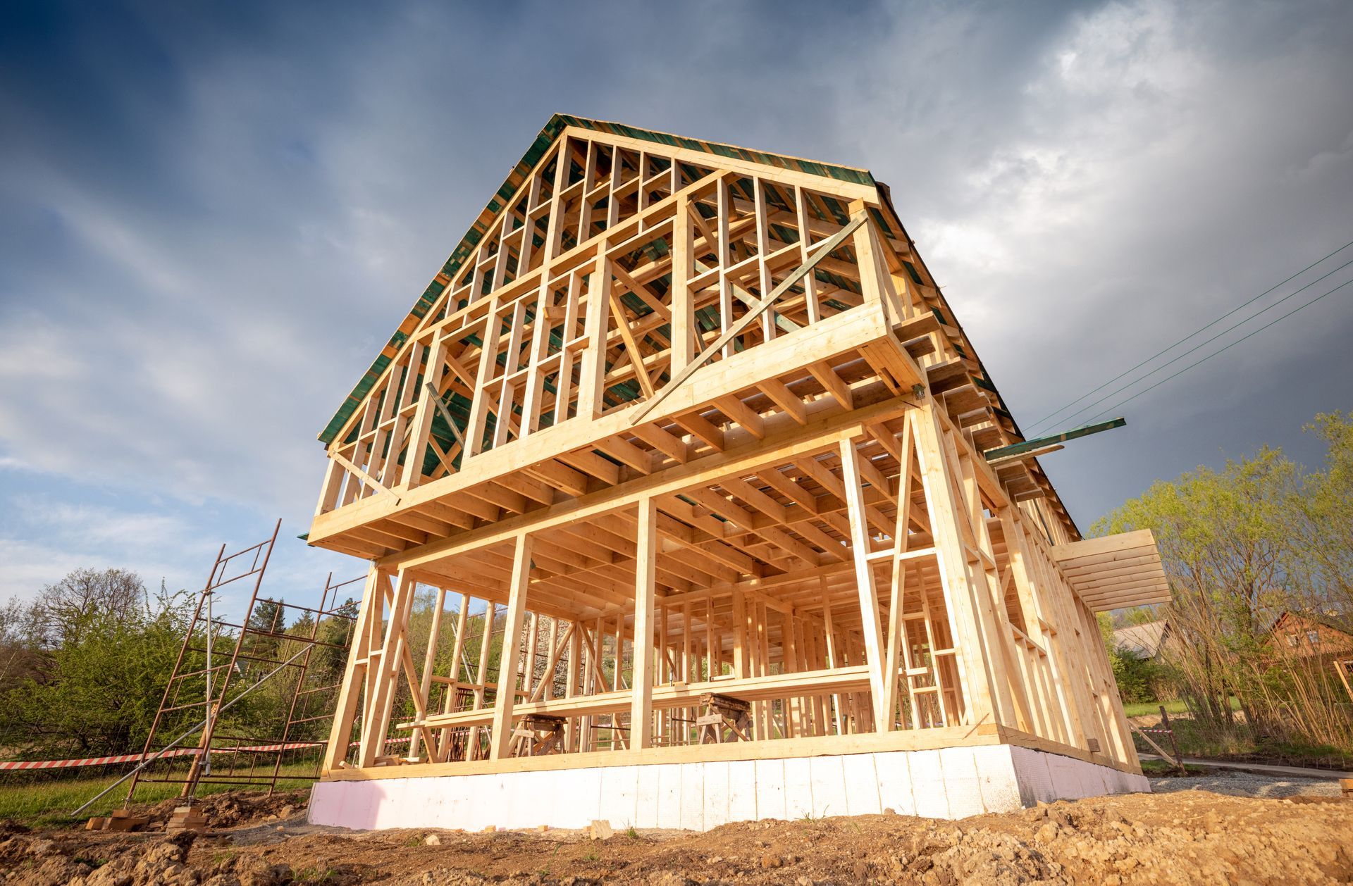 Wooden house frame under construction, against a cloudy sky.