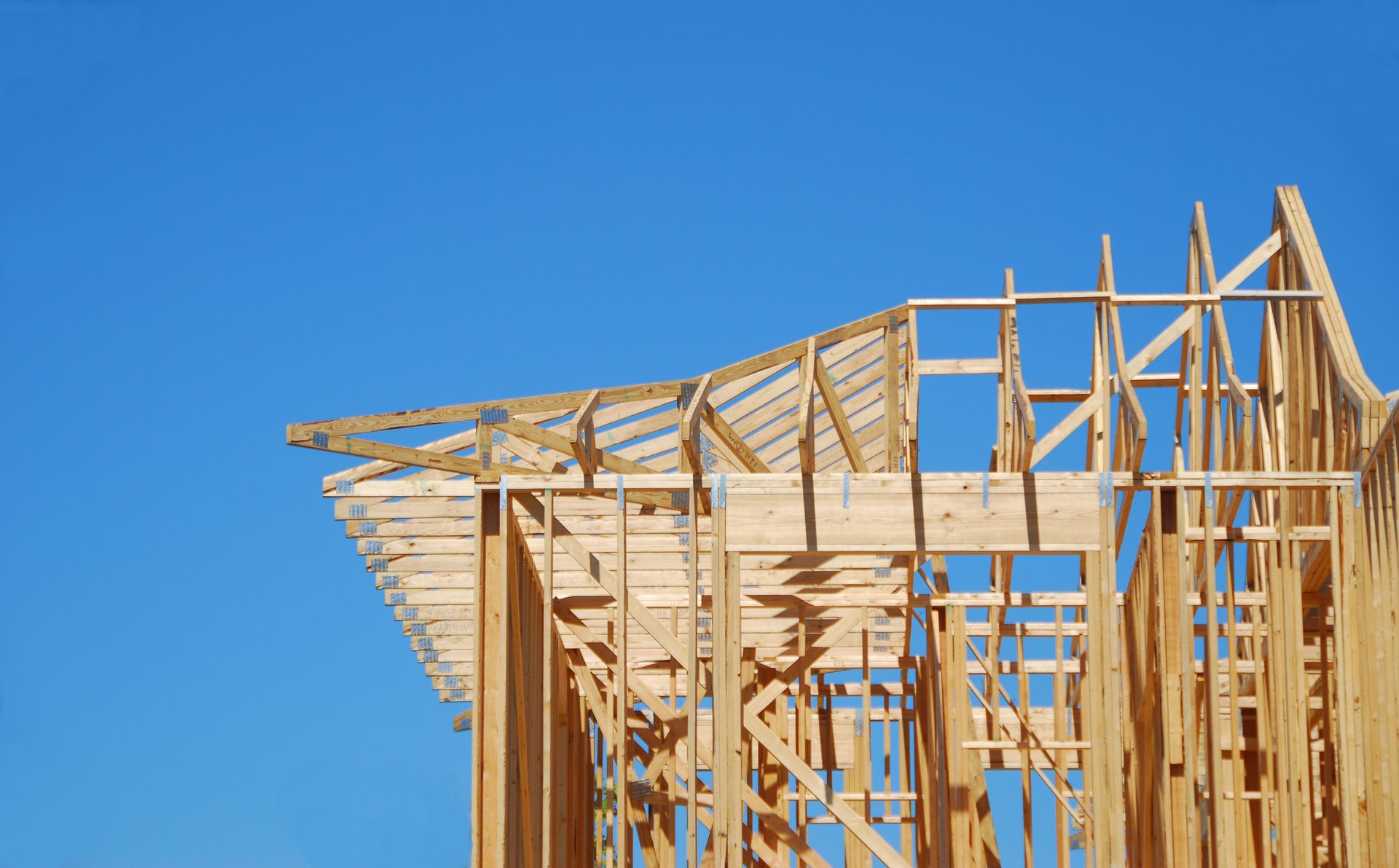 Wooden house frame against a bright blue sky, partially constructed.