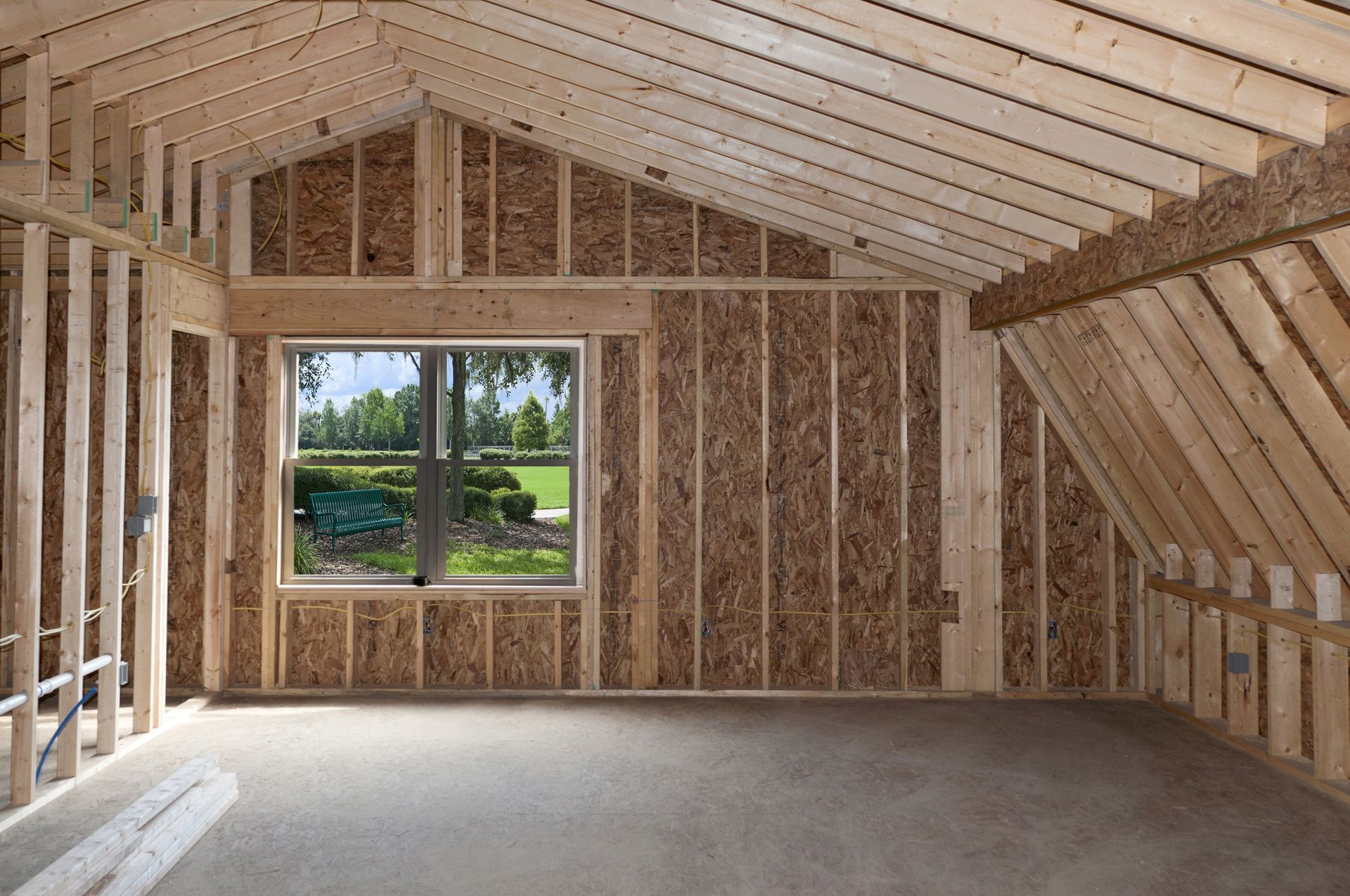 Interior of a room under construction, with wooden frame, window, and exposed Oriented Strand Board walls.