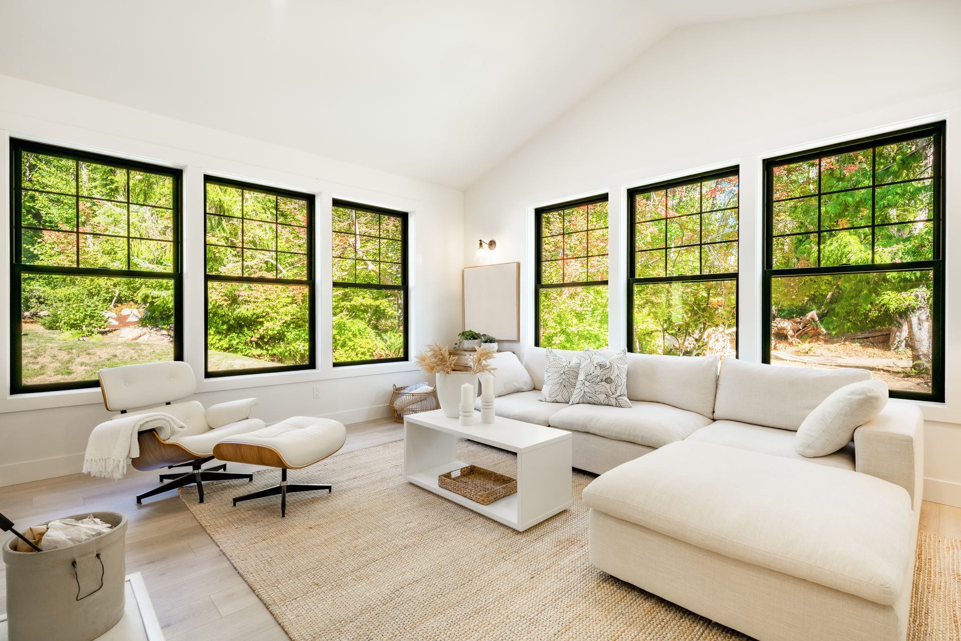 Bright, white living room with large windows, white couch, and neutral rug.