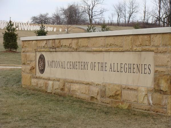 Sign for the National Cemetery of the Alleghenies, with a background of white headstones.