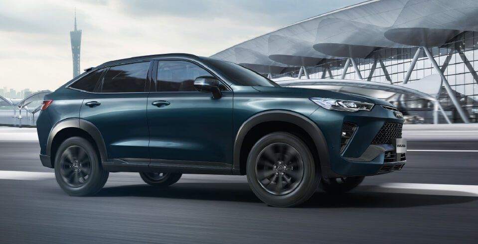 SUV Haval color verde azulado oscuro estacionado en una carretera pavimentada, con arquitectura moderna en el fondo.
