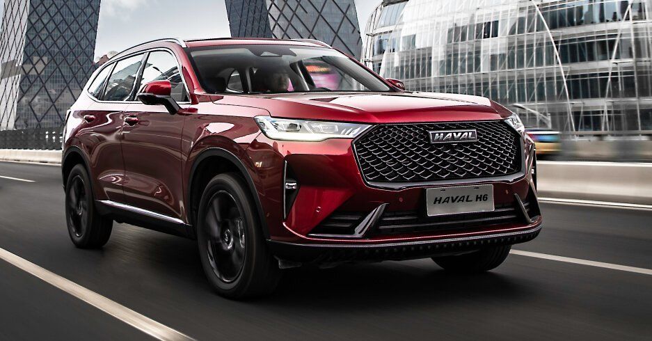 SUV Haval de color rojo circulando por una carretera frente a edificios modernos.