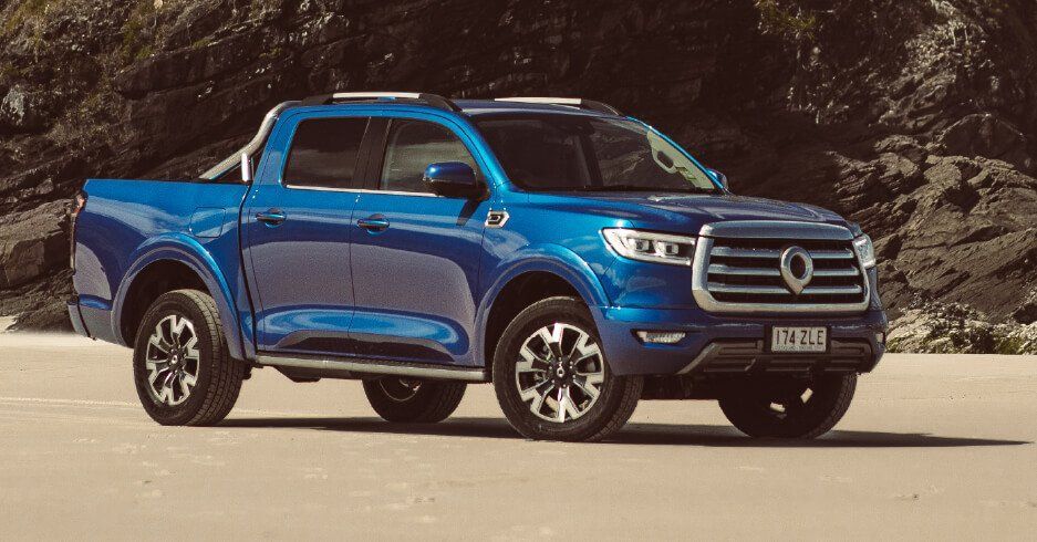 Camioneta azul estacionada en una playa, contra un fondo rocoso.