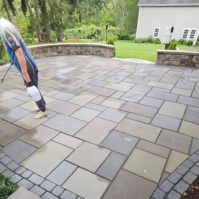 Person installing large stone pavers on an outdoor patio beside a lawn and house