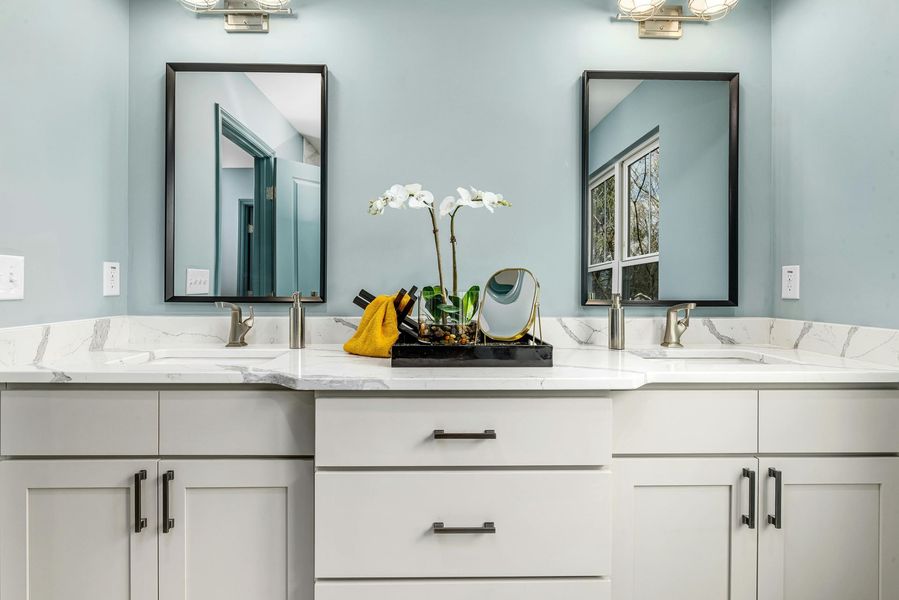 Bathroom with two sinks, mirrors, white cabinets, and light blue walls.