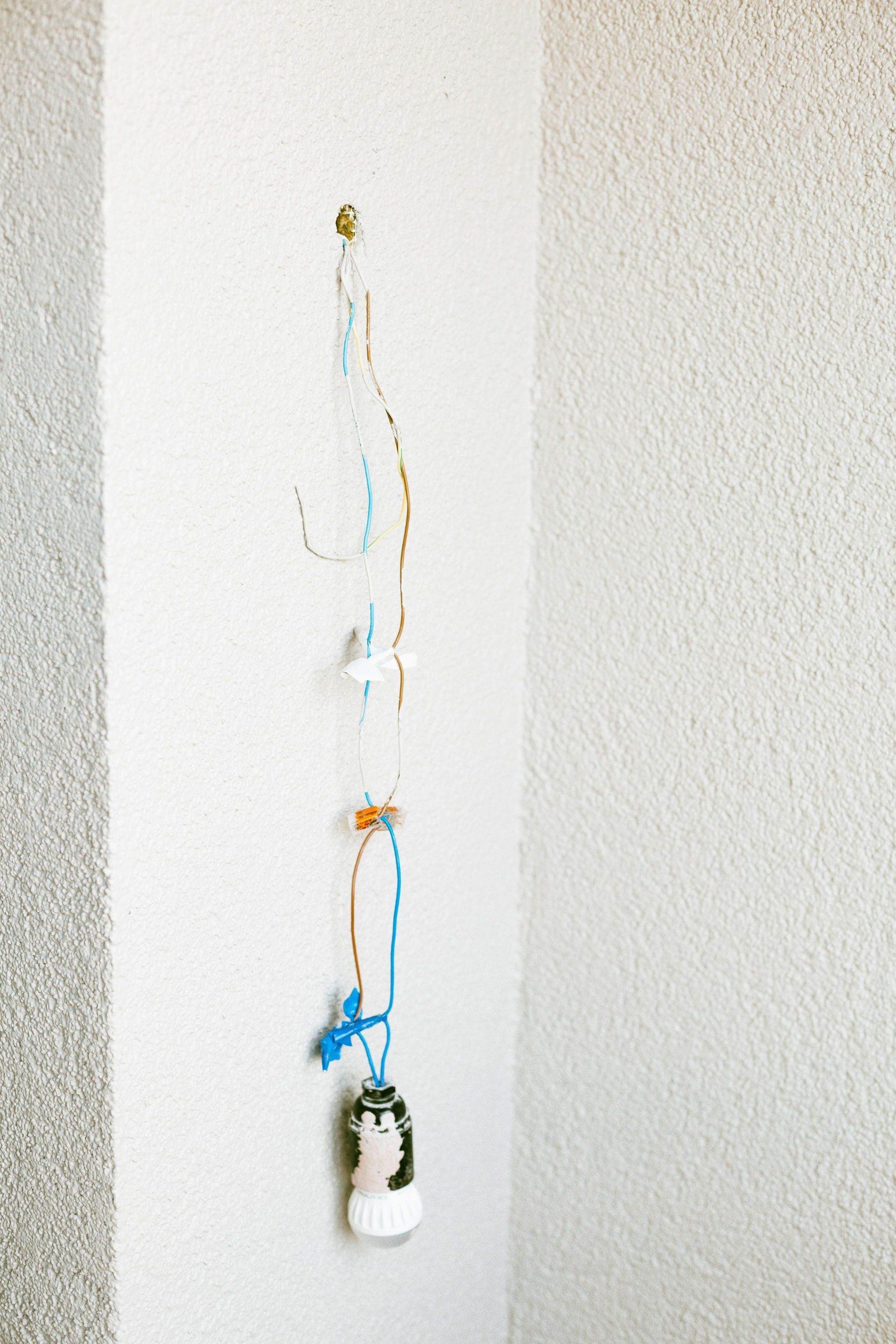 A handmade wind chime hanging on a white corner wall. It has beads, string, and a small figurine.