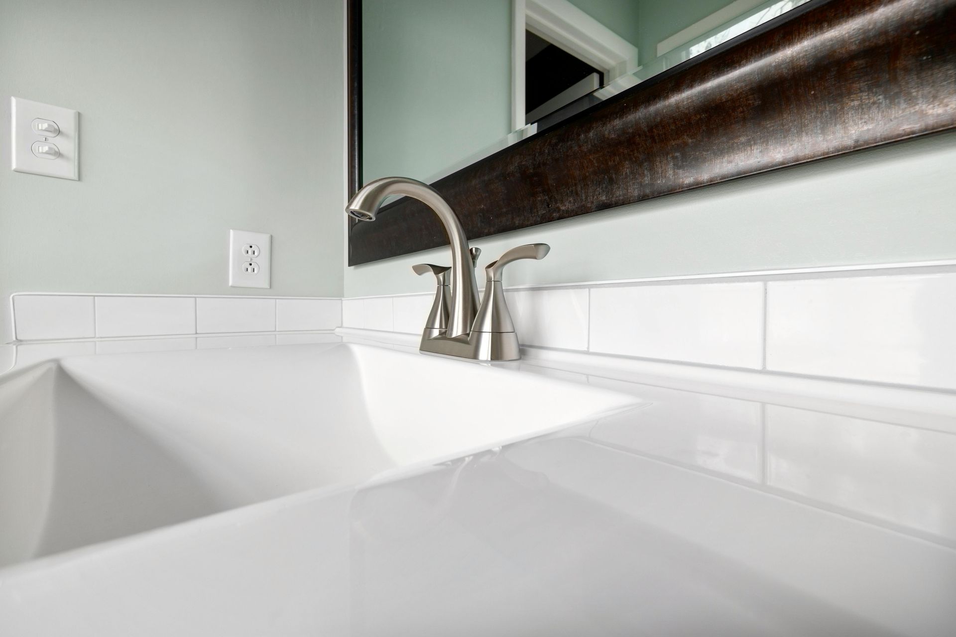 White bathroom sink with silver faucet, white tiled backsplash, and mirror.