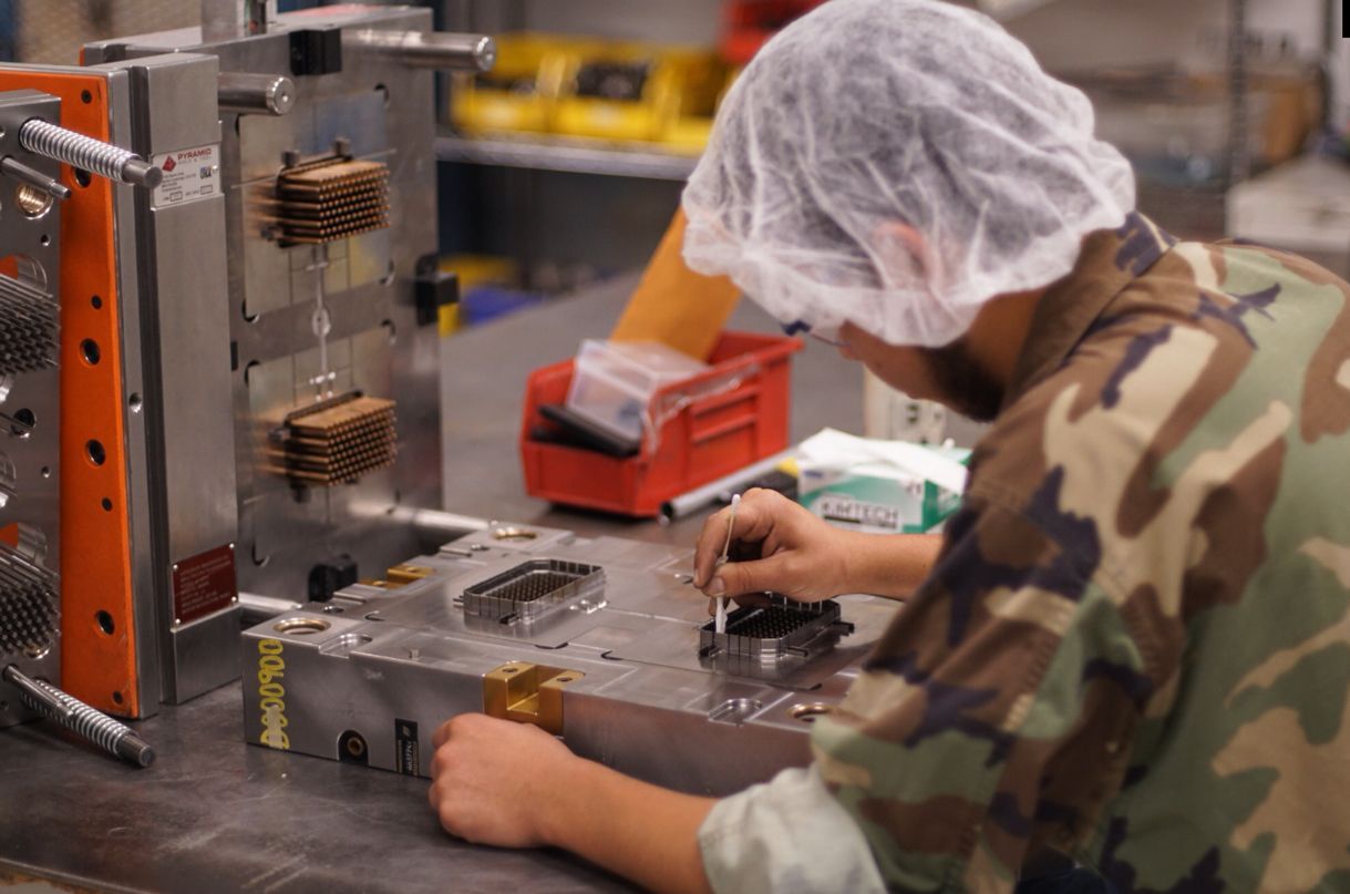 A person in a camouflage uniform  working on a machine in a factory