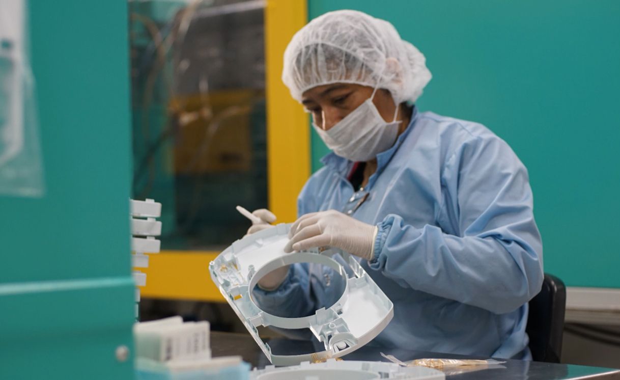 A woman wearing a mask and gloves is working on a piece of plastic