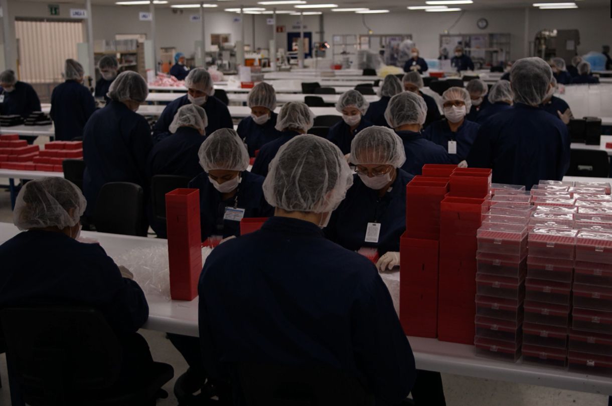 A group of people wearing hair nets and masks are working in a factory