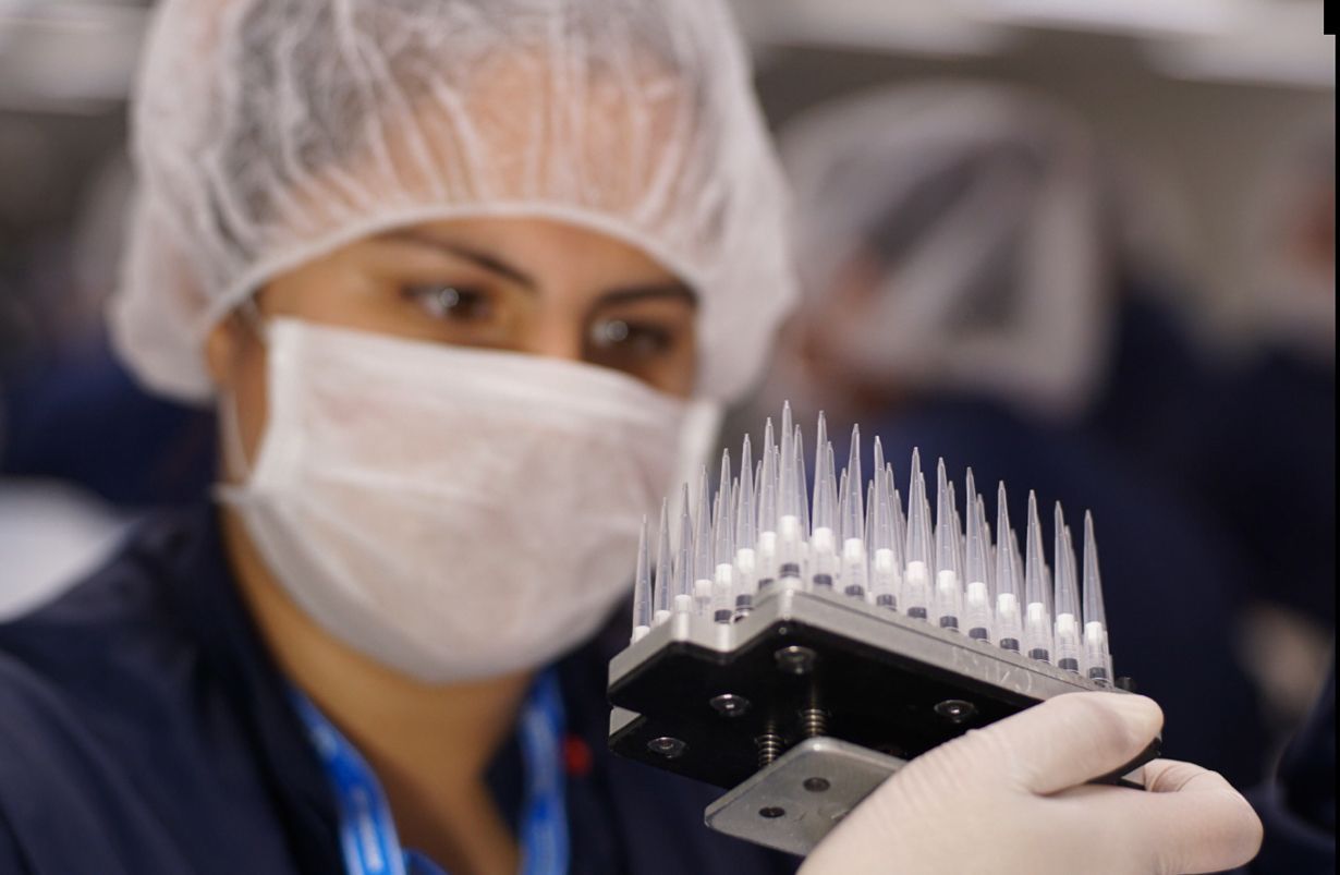 A woman wearing a mask and gloves is holding a pipette