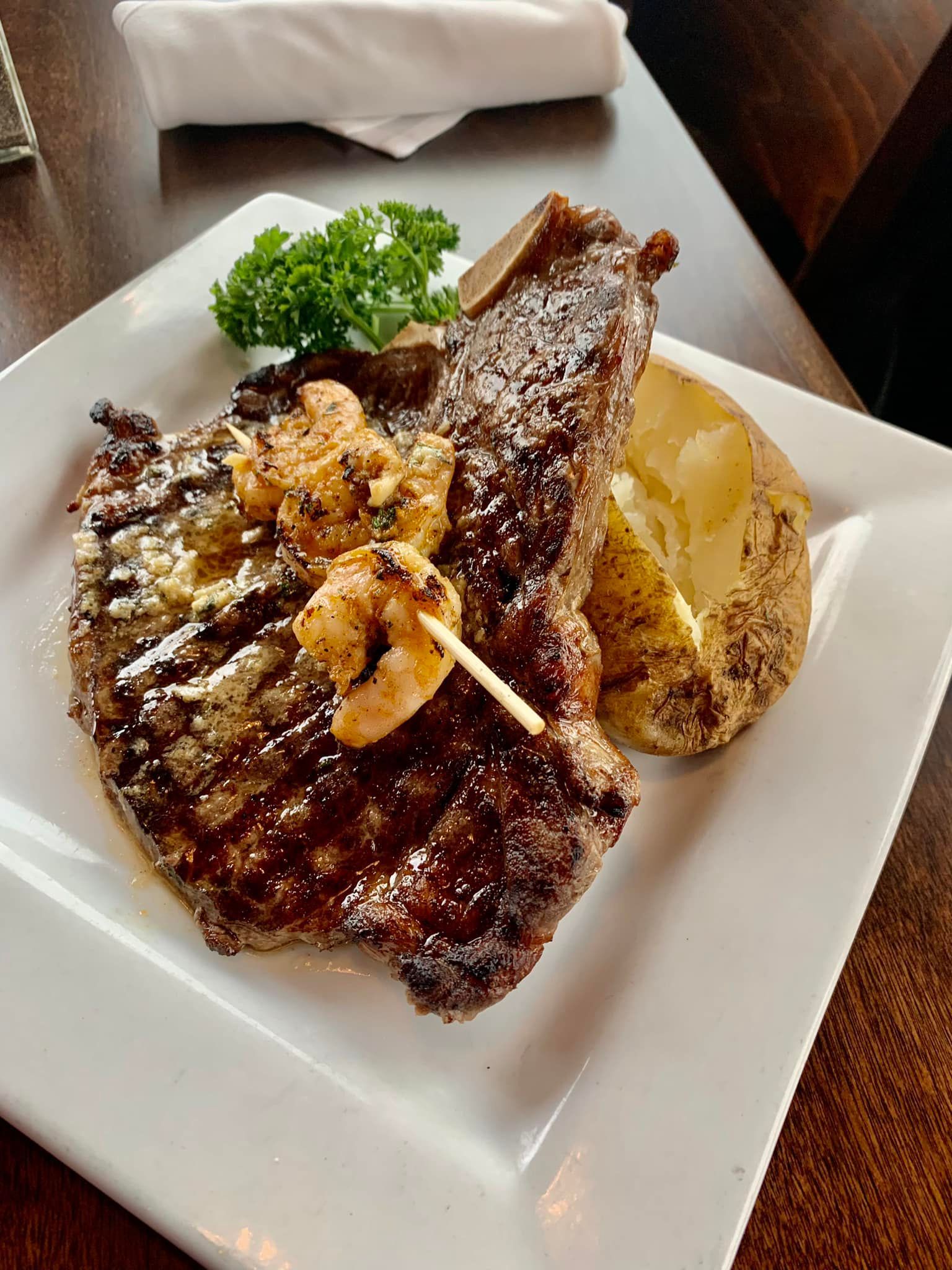 T-Bone Steak with Blackened Shrimp topped with cowboy butter served with a baked potato.