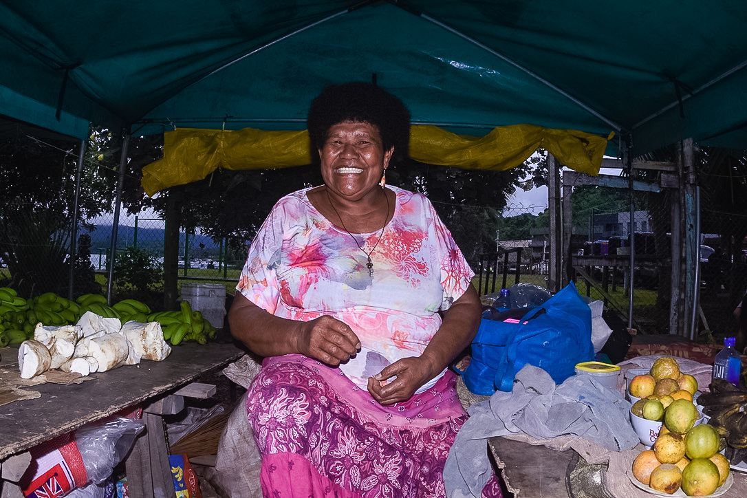 A smiling Fijian lady dressed in pink and white under a tarpaulin