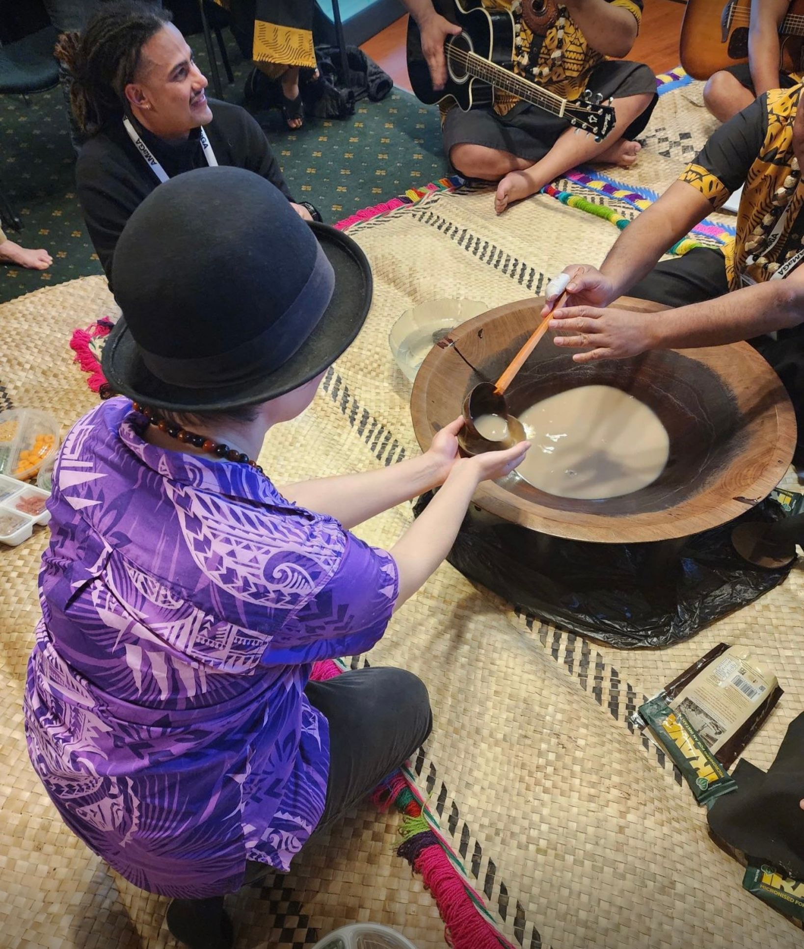 A wooden kava bowl filled with a milky liquid being offered to a guest at the ceremony