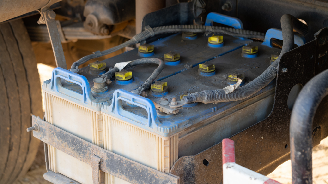 Two truck batteries secured in a metal frame, with blue tops and yellow terminals.