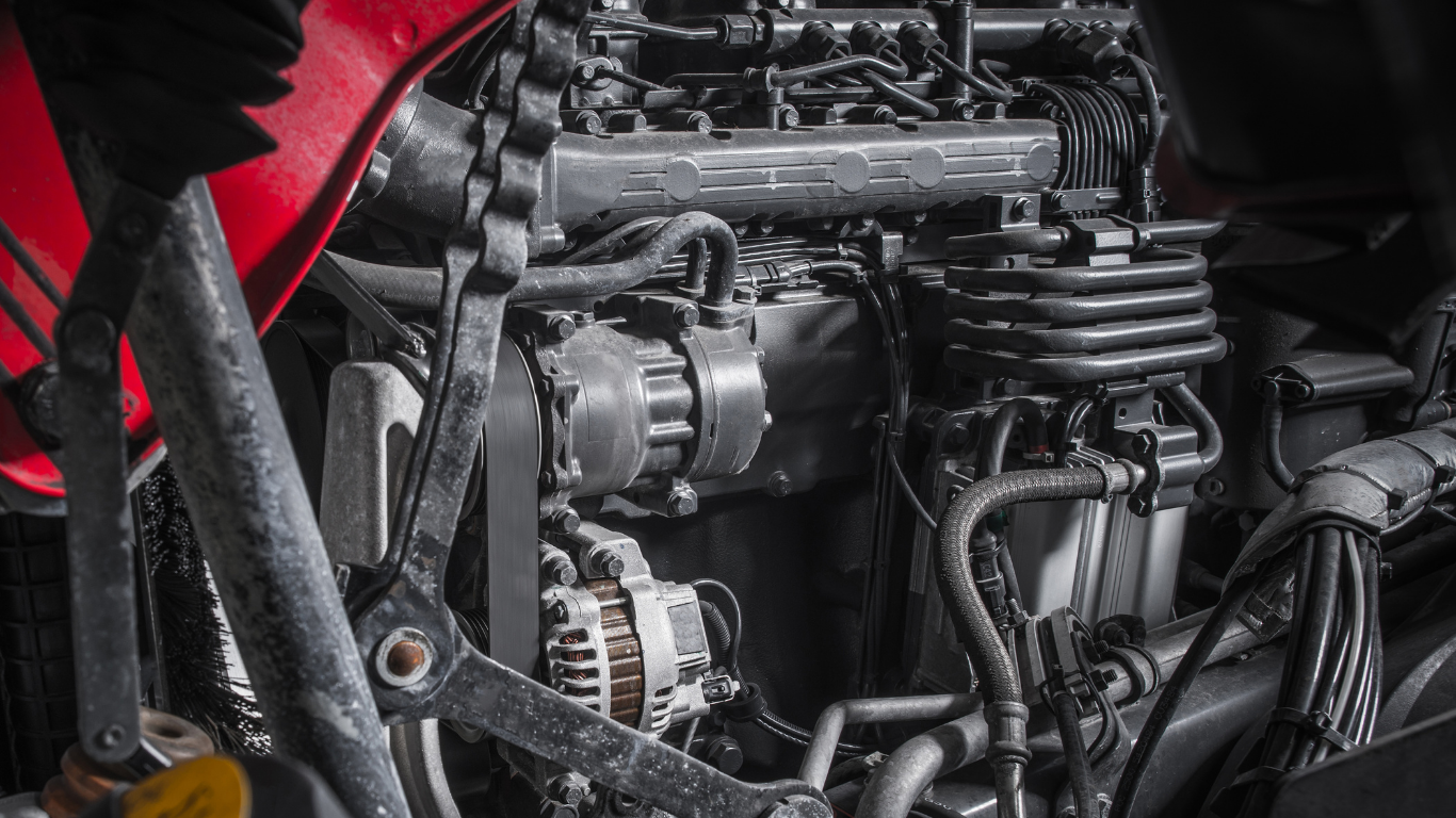 Close-up view of a black tractor engine with metal components and attached belts. Red frame on the left.