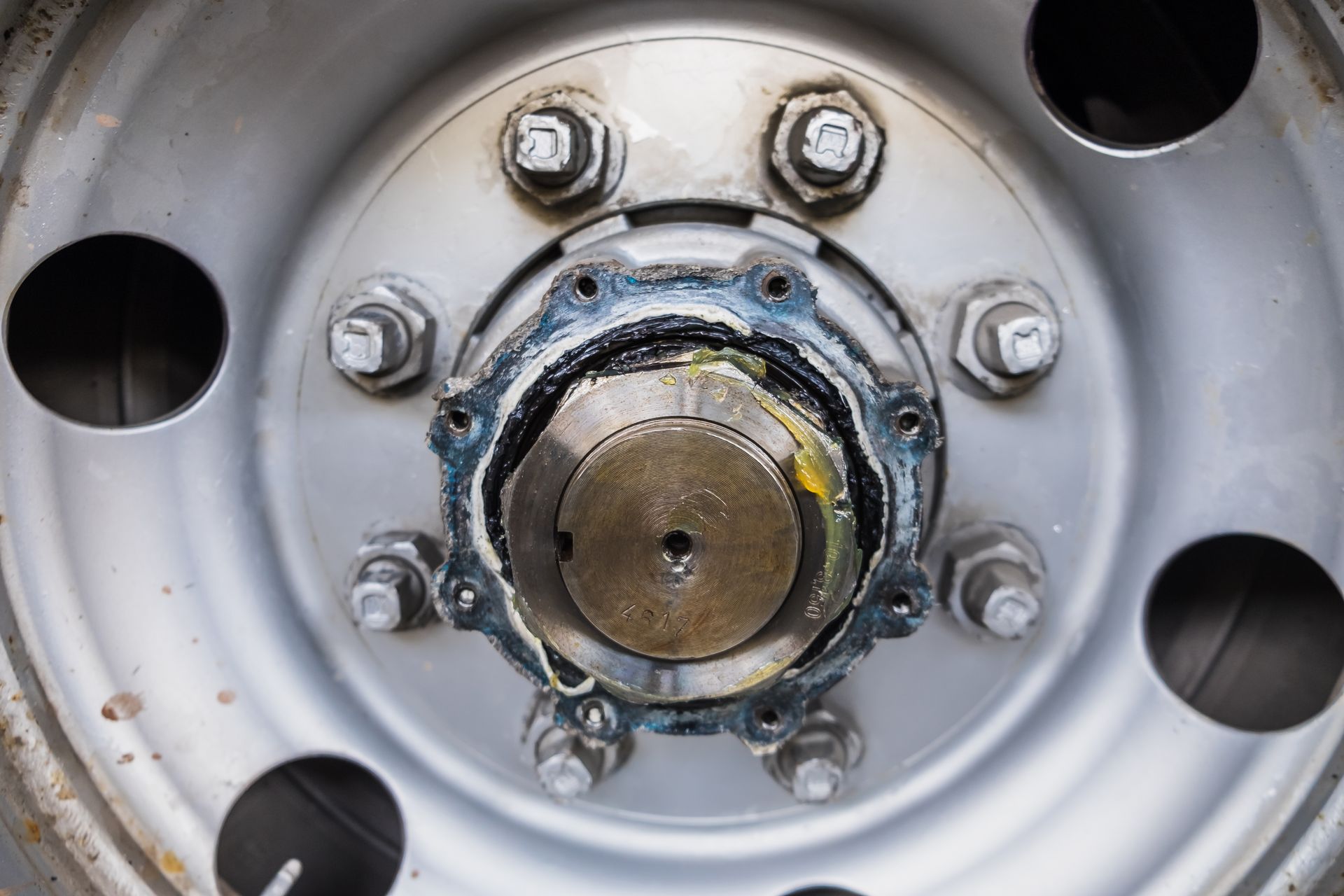 Close-up of a silver truck wheel hub with visible lug nuts and a center cap covered in grease.