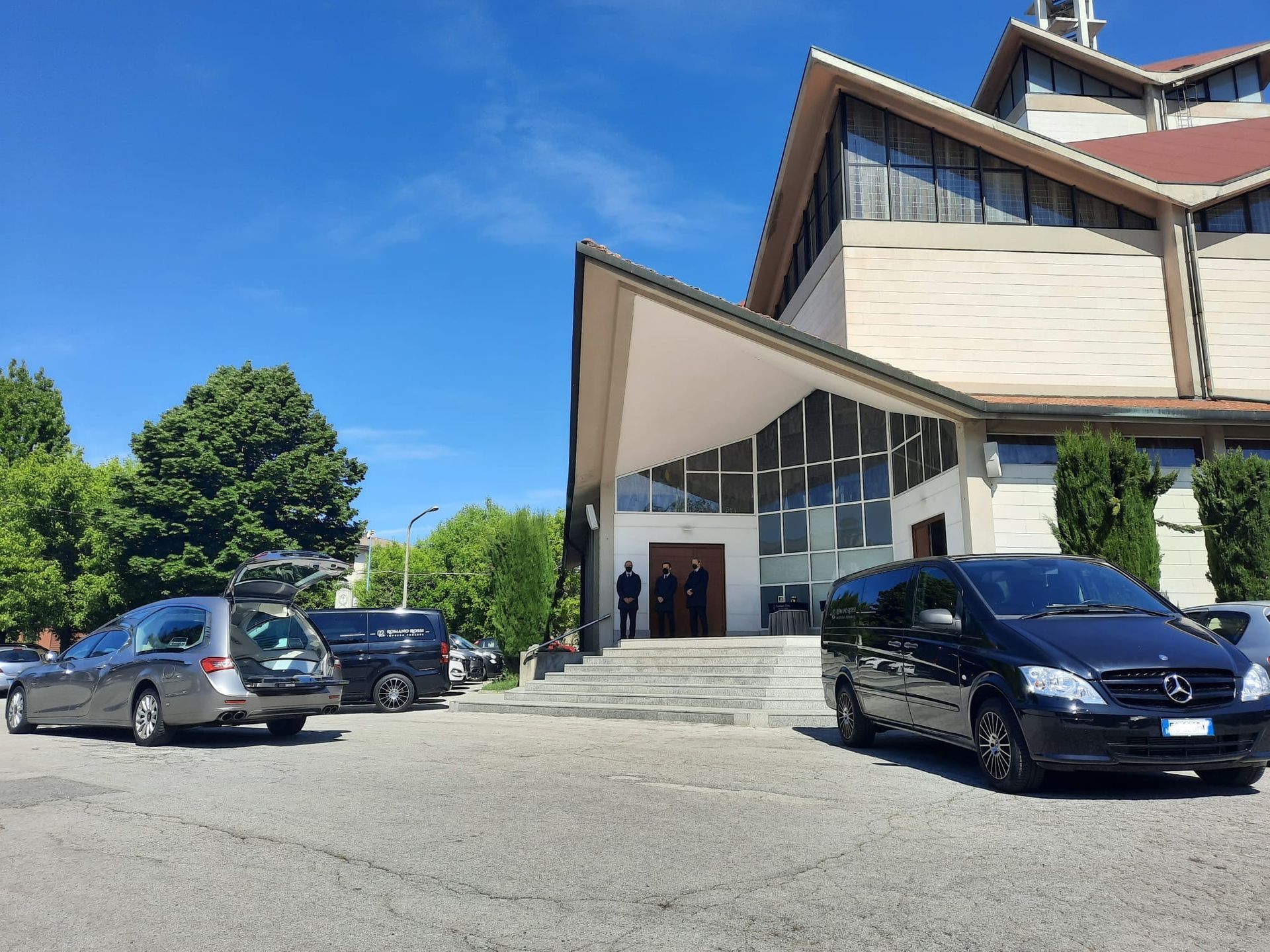 Un gruppo di carri funebri è parcheggiato davanti a una chiesa.