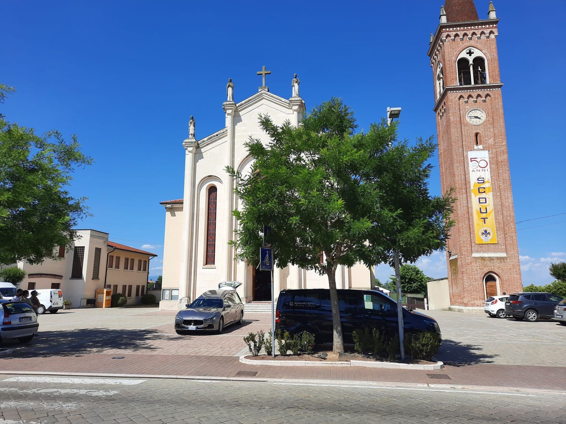 Una chiesa con una torre dell'orologio e delle auto funebri