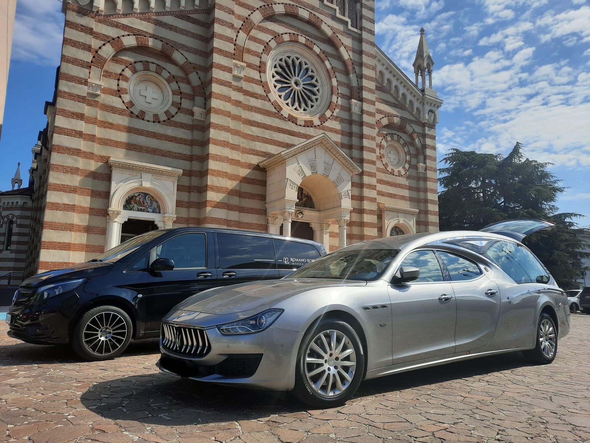 Due auto funebri sono parcheggiate davanti a una chiesa.
