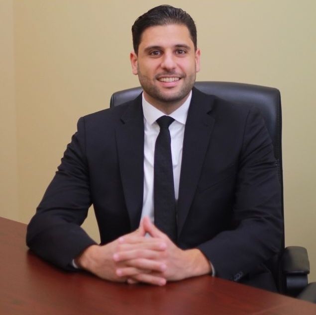 A man in a suit and tie is sitting at a desk with his hands folded