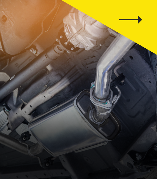 Underside view of a car showing exhaust system components, including a muffler and piping, against a blurred background.