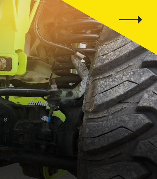 Close-up of a lifted off-road vehicle's wheel, showing suspension components, a black tire, and a yellow accent.