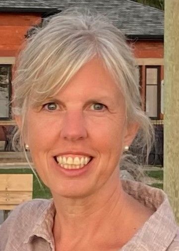 Smiling woman with blonde hair, light skin, and a beige top, in front of a building.