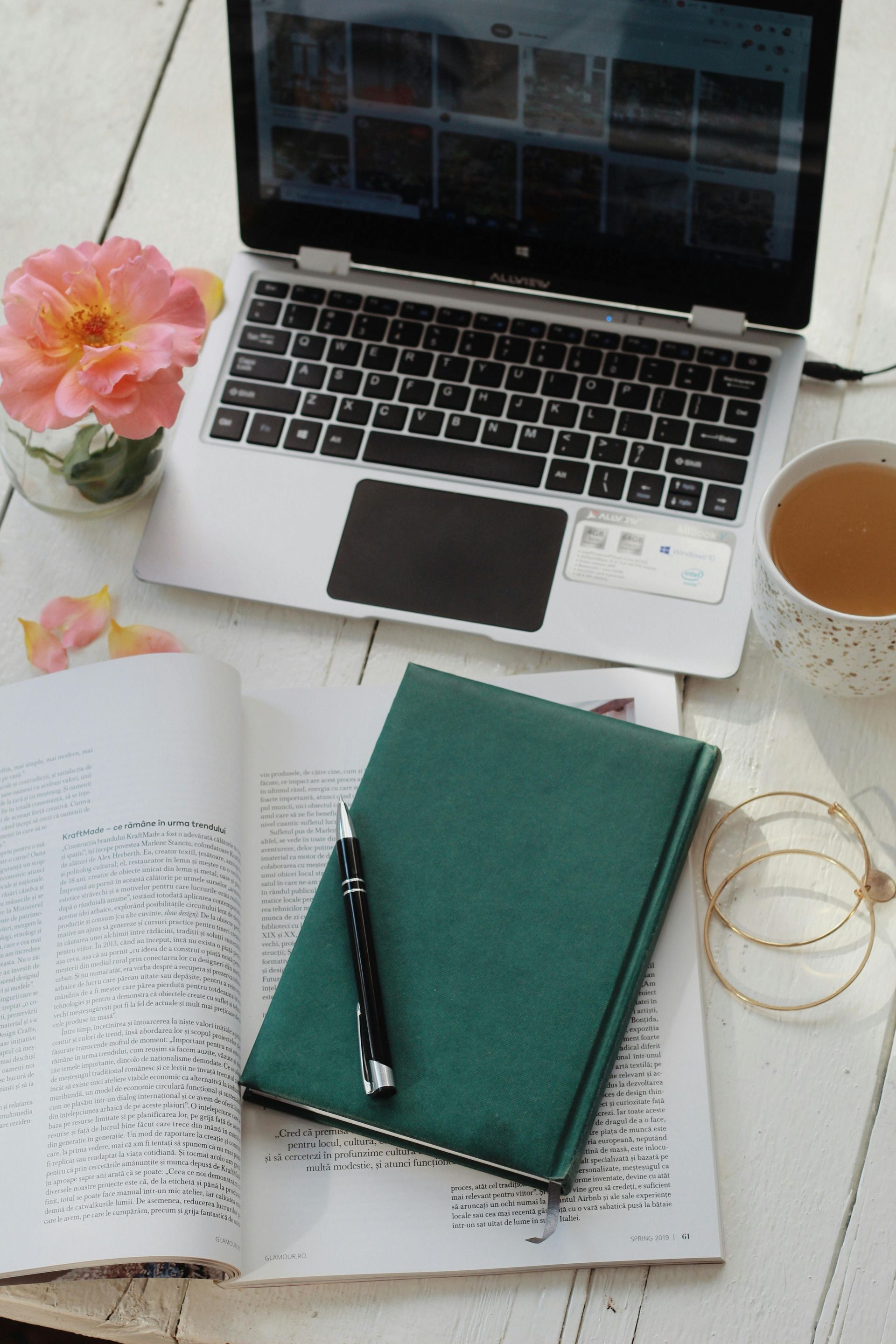 Laptop and notebook on white wooden desk, flower and tea cup.